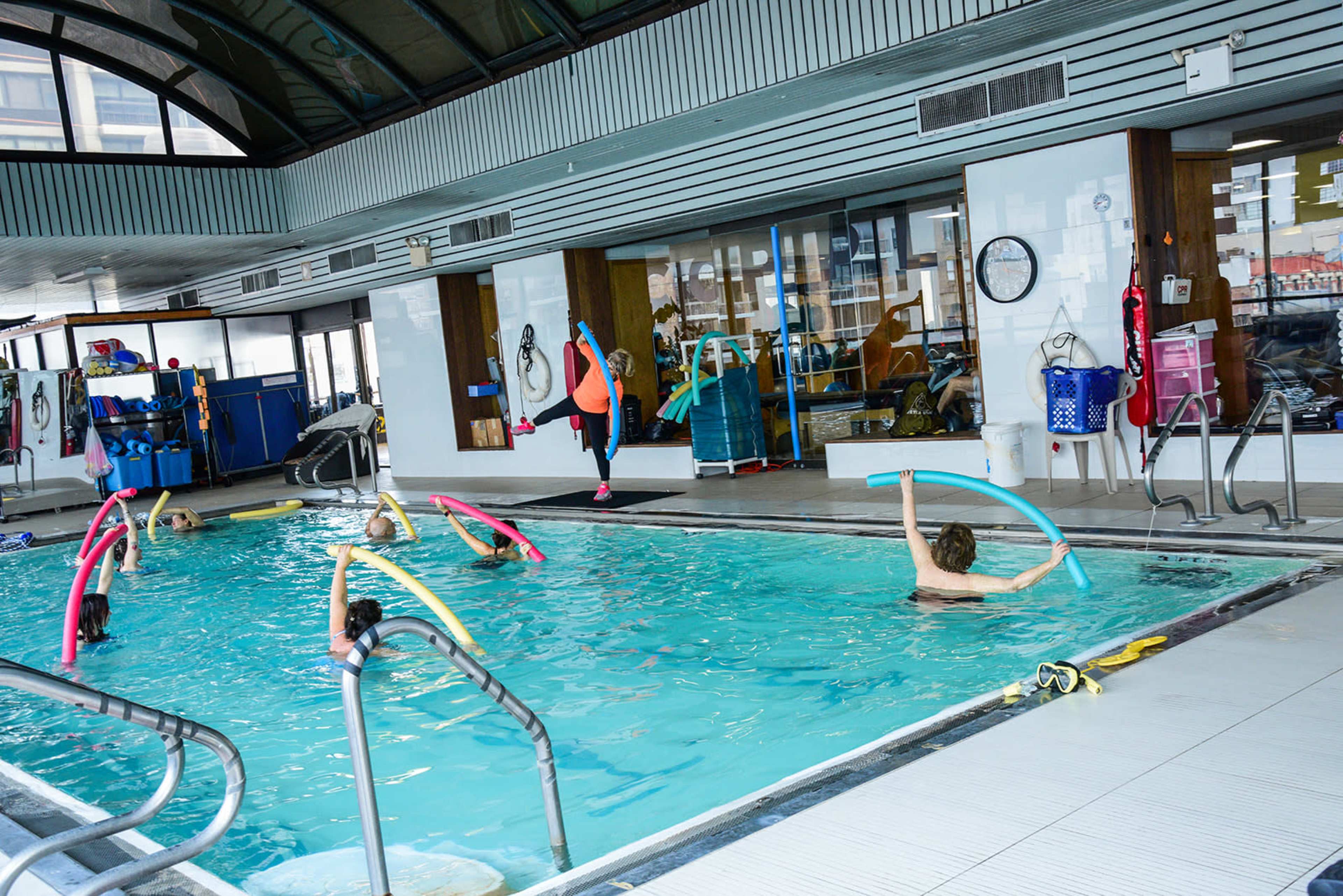 A group of people participates in a water aerobics class inside a pool facility.