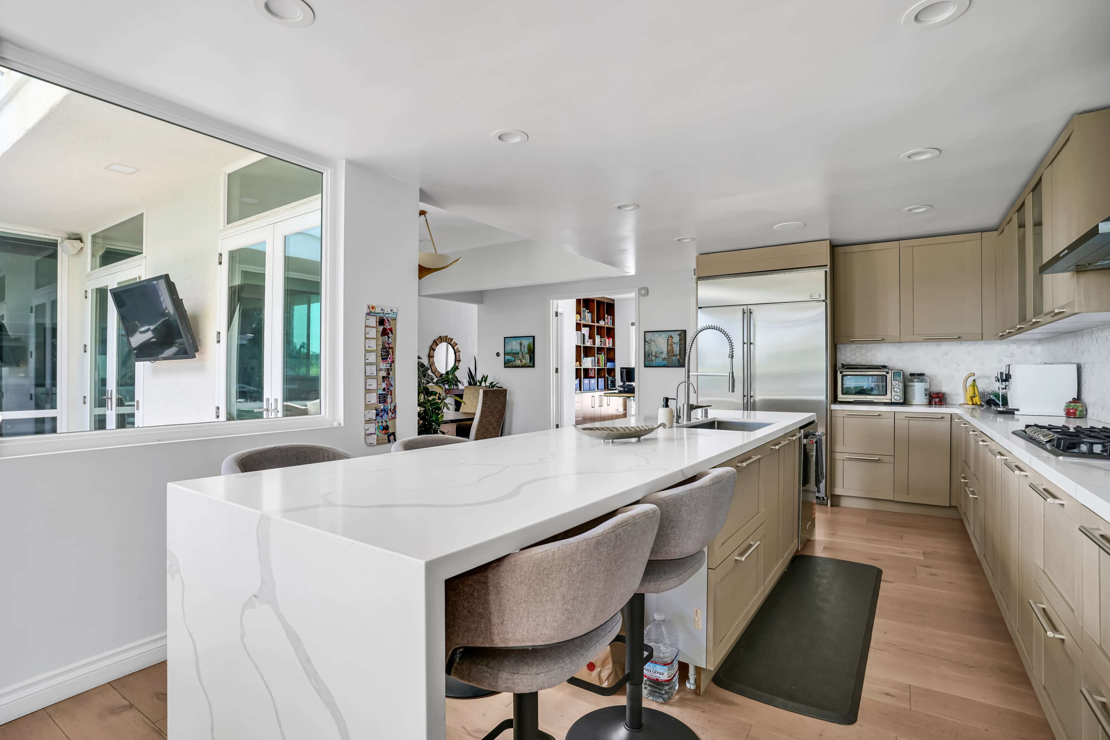 The image shows a modern kitchen featuring a large island with bar seating, sleek cabinetry, and stainless steel appliances.