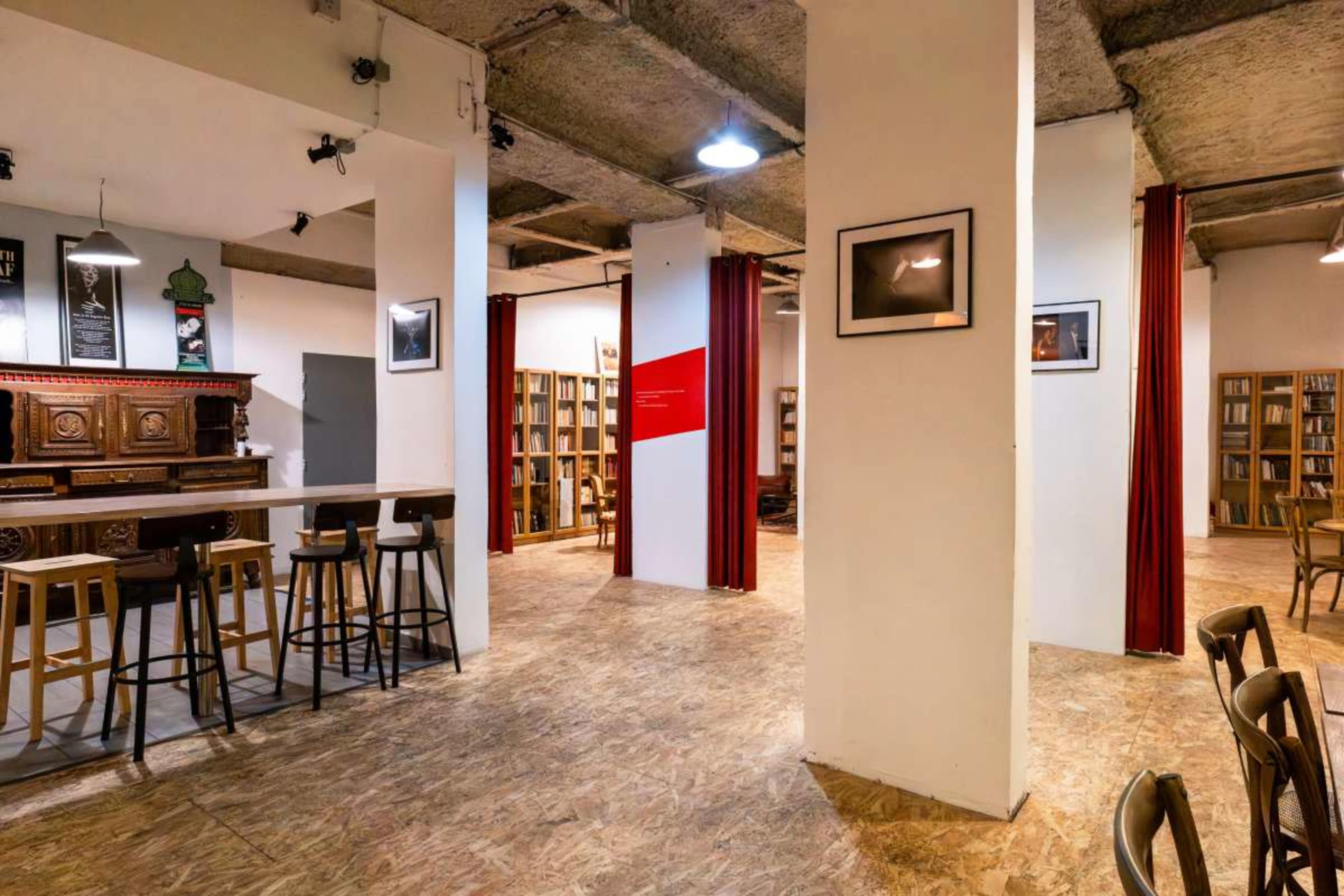 The image shows an interior space with a bar area and bookshelves, featuring wooden stools and white walls.