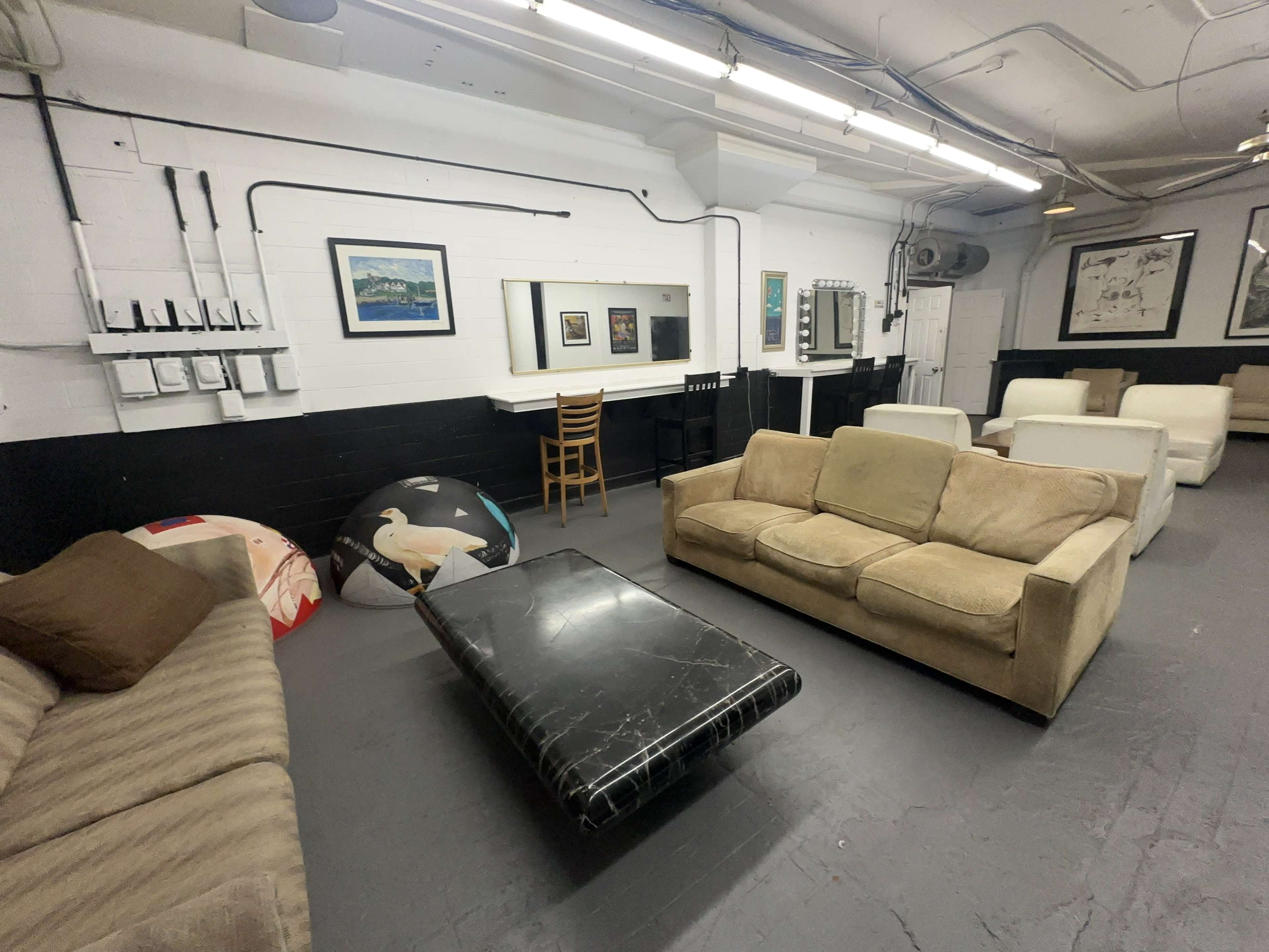 A spacious room with several sofas, a low coffee table, and a chair against the wall, featuring framed artwork and a mirrored vanity area.