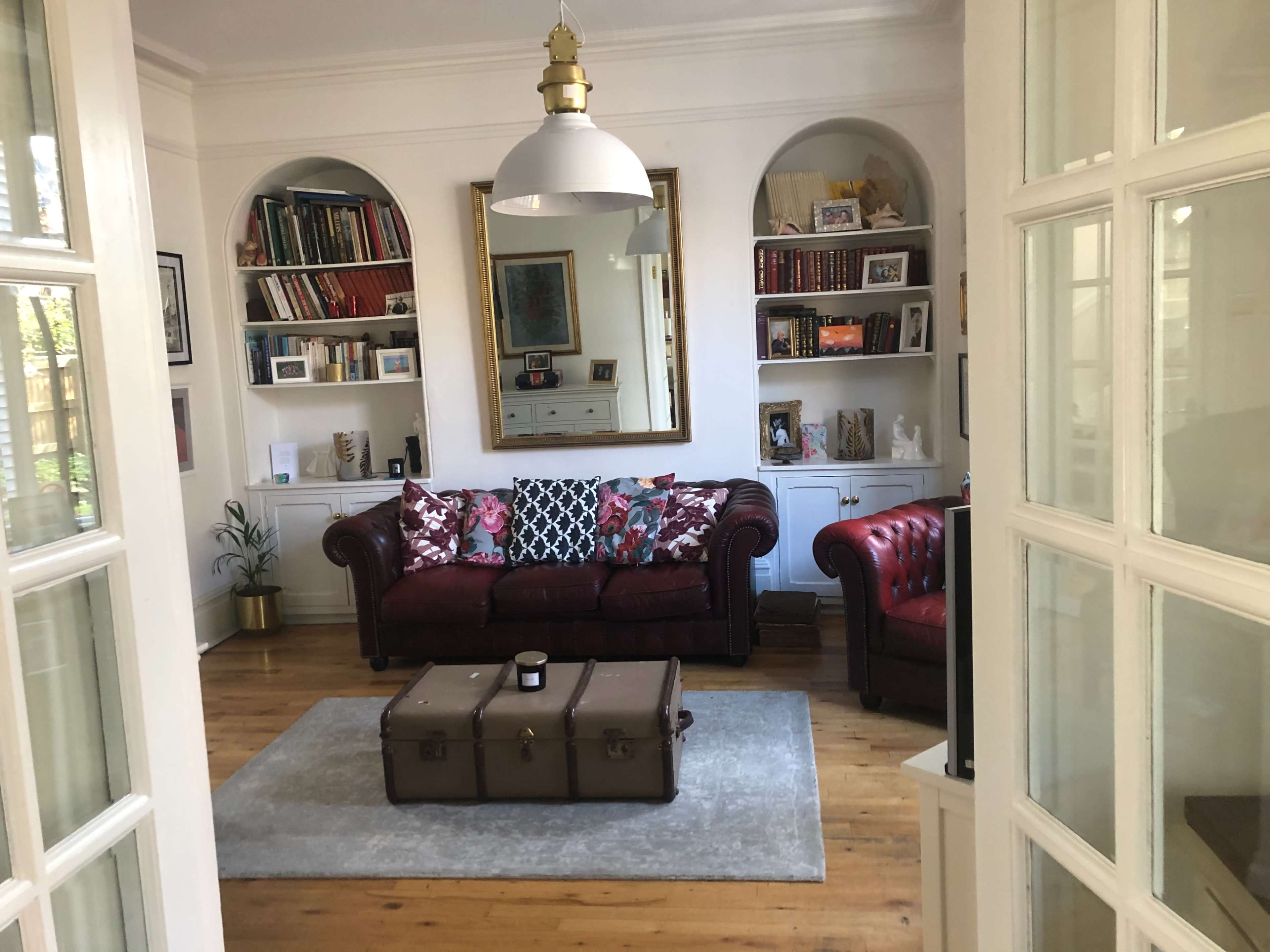 A living room with a red leather sofa, a coffee table, and bookshelves filled with books and decorative items.