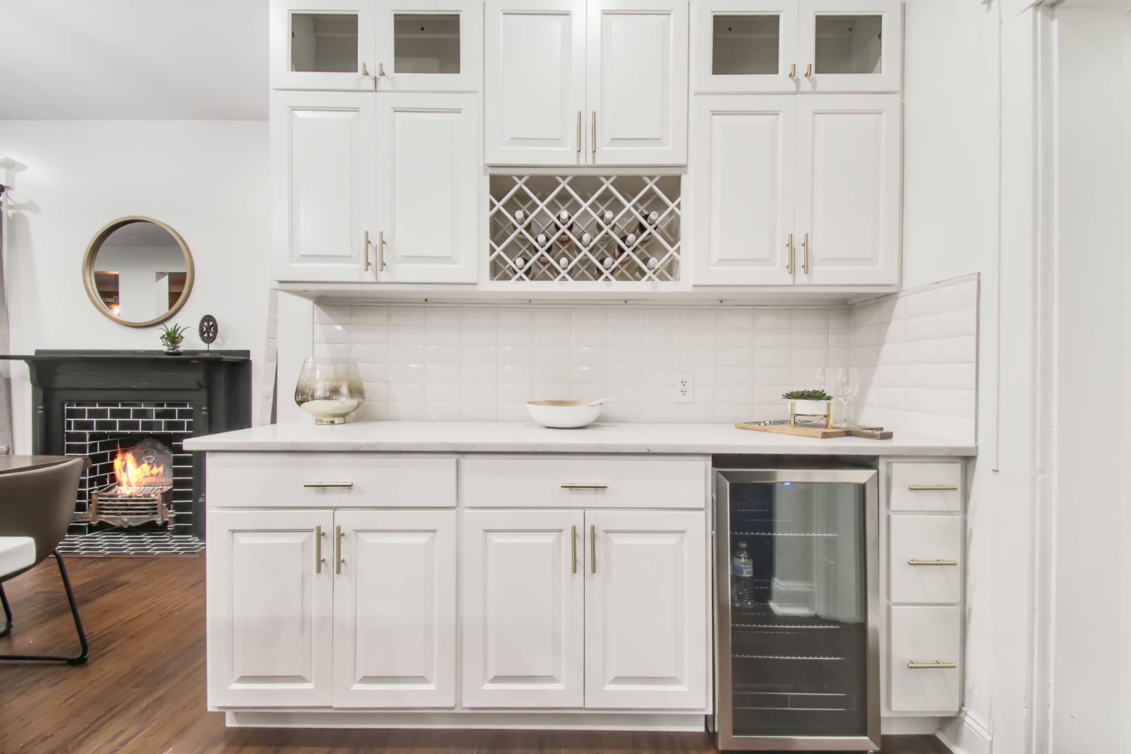 A modern kitchen area with white cabinetry, a wine rack, and a small wine refrigerator beneath the counter.