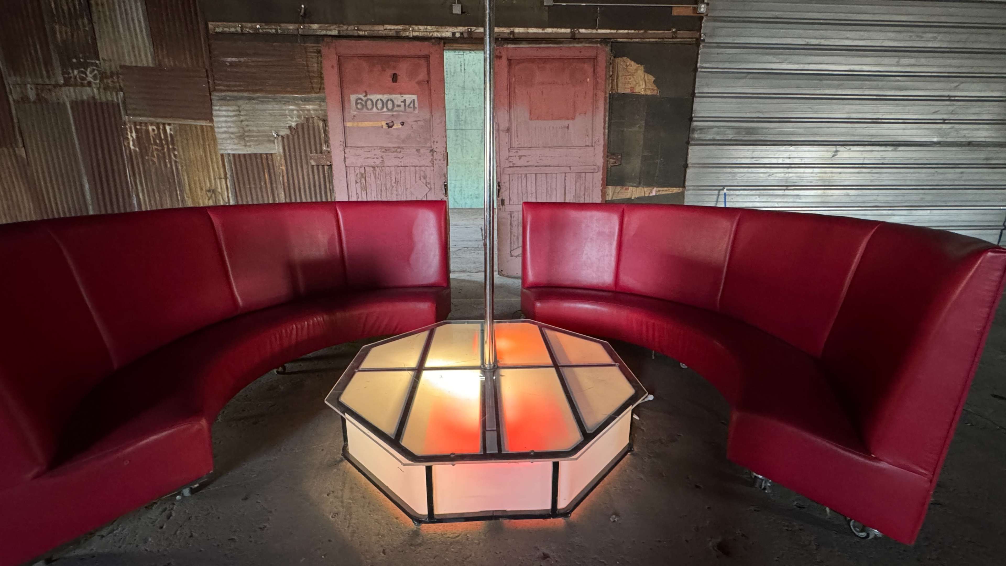 The image shows a circular seating area with red curved couches surrounding a hexagonal, illuminated table in an urban setting.