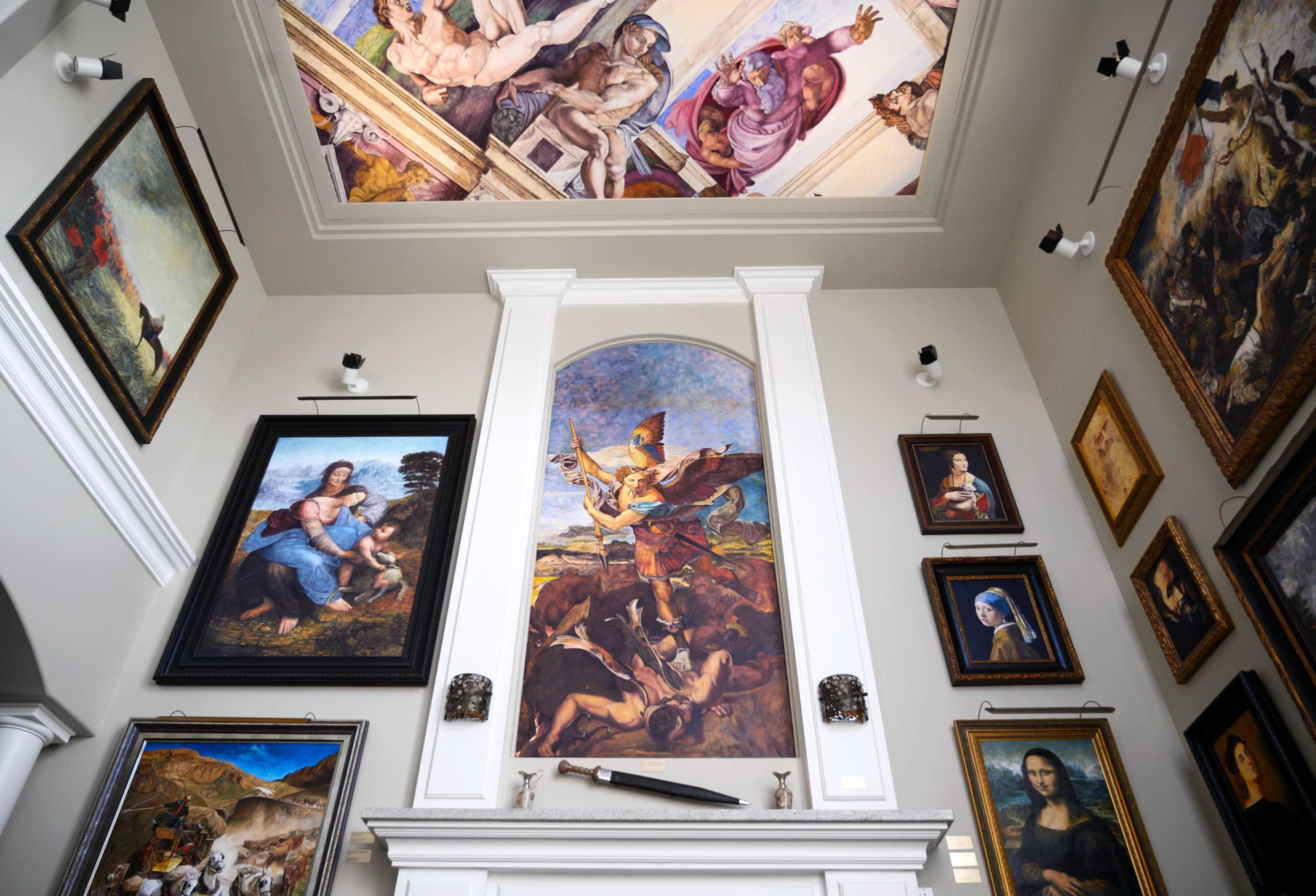 The image shows a gallery wall featuring a variety of framed artworks, including paintings, with a mural on the ceiling depicting a historical scene.