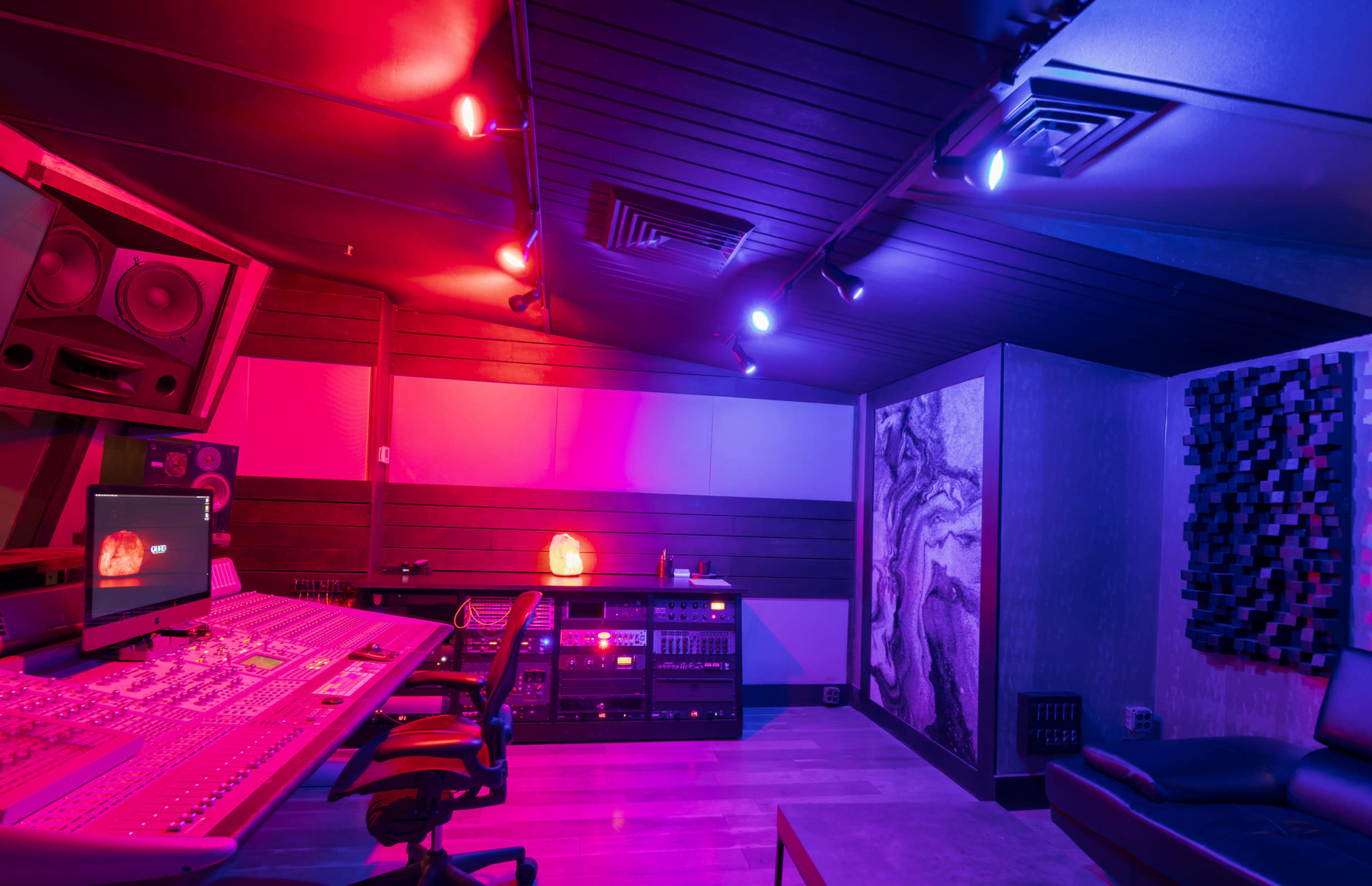 The image shows a dimly lit music studio featuring sound equipment, a mixing console, and colorful LED lighting.