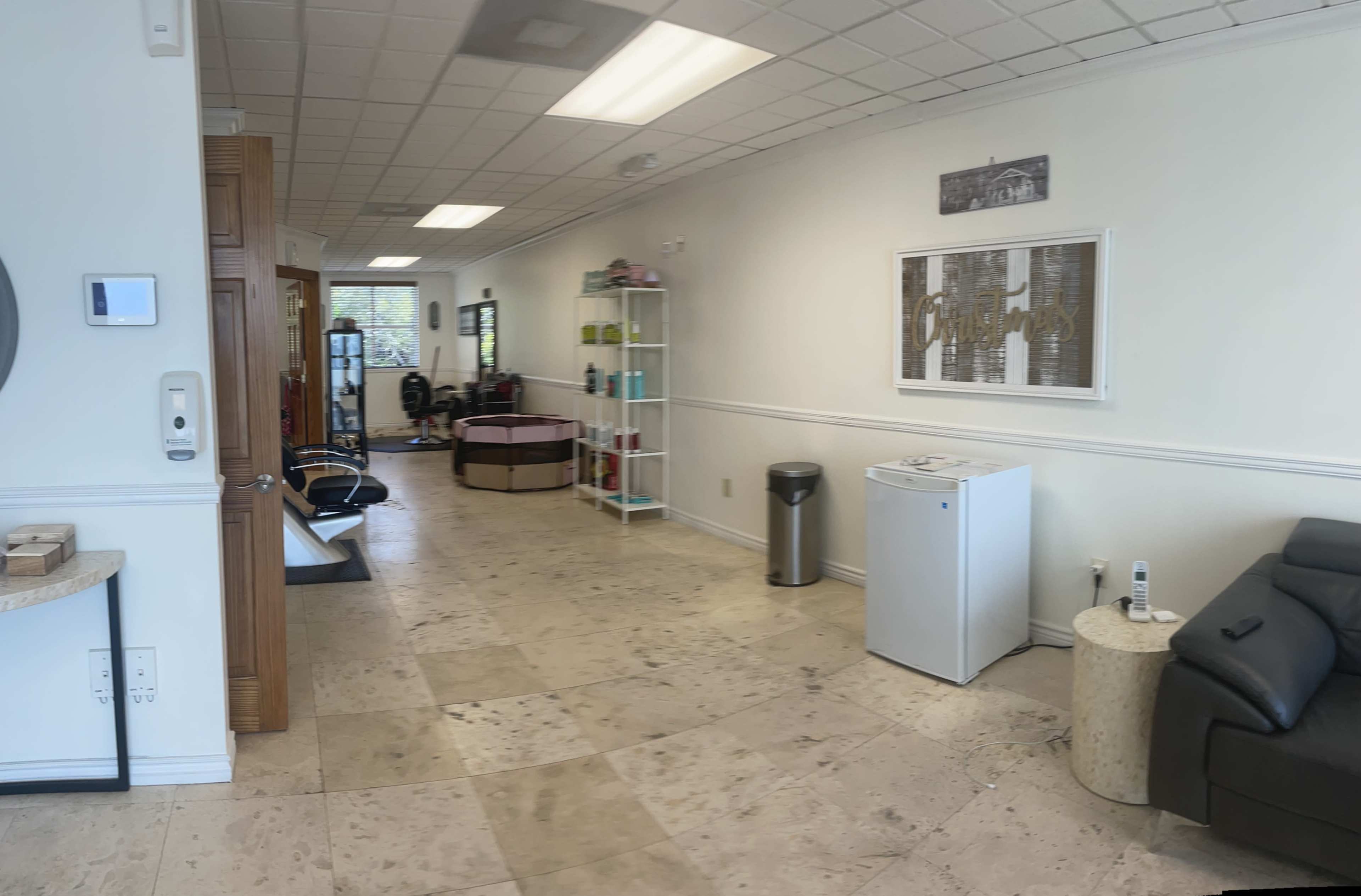 A spacious, well-lit room with tiled flooring, featuring a reception area, seating, and shelves against the walls.