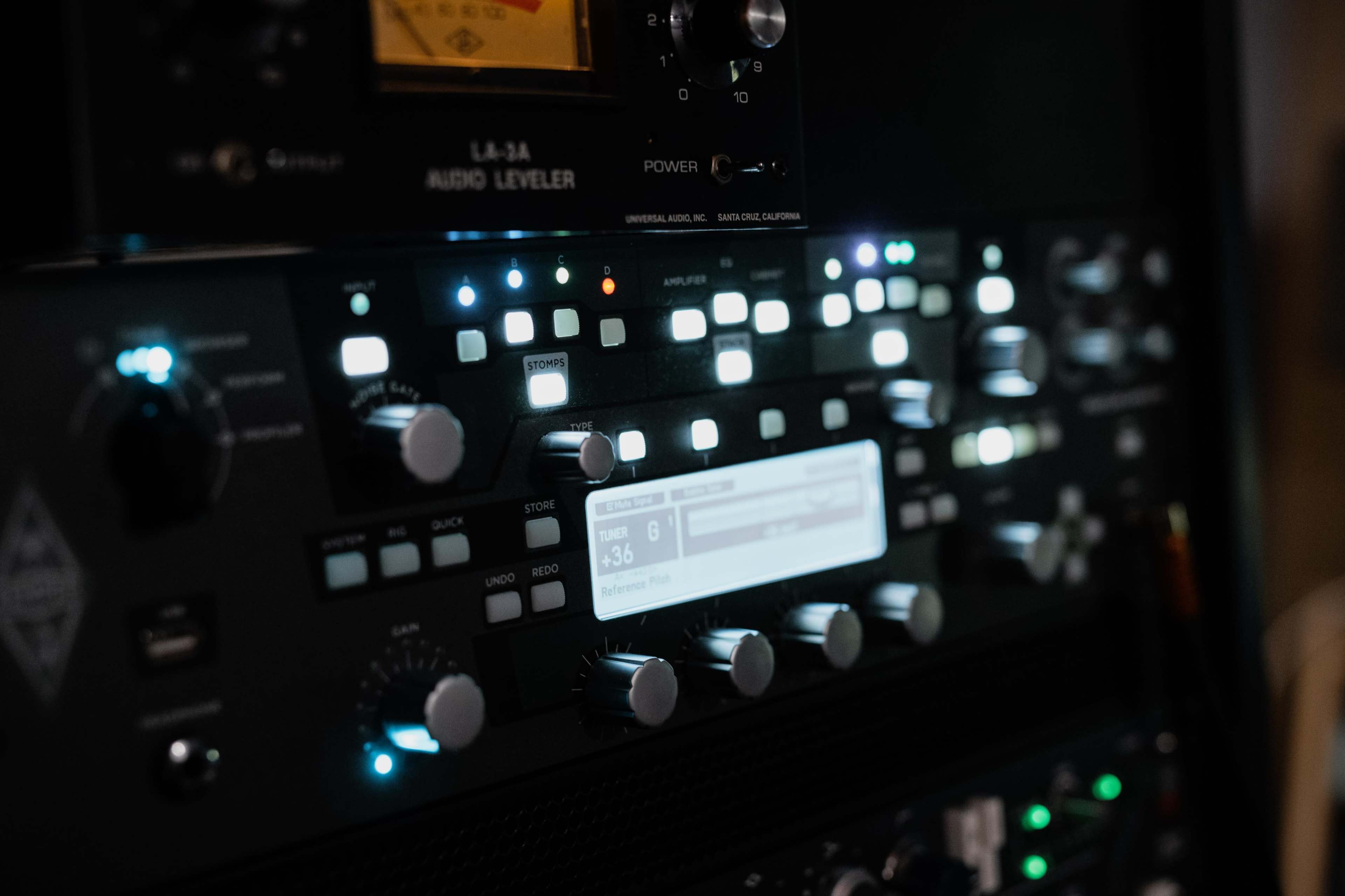 A close-up of a rack-mounted audio equipment panel featuring various knobs, buttons, and illuminated indicators.