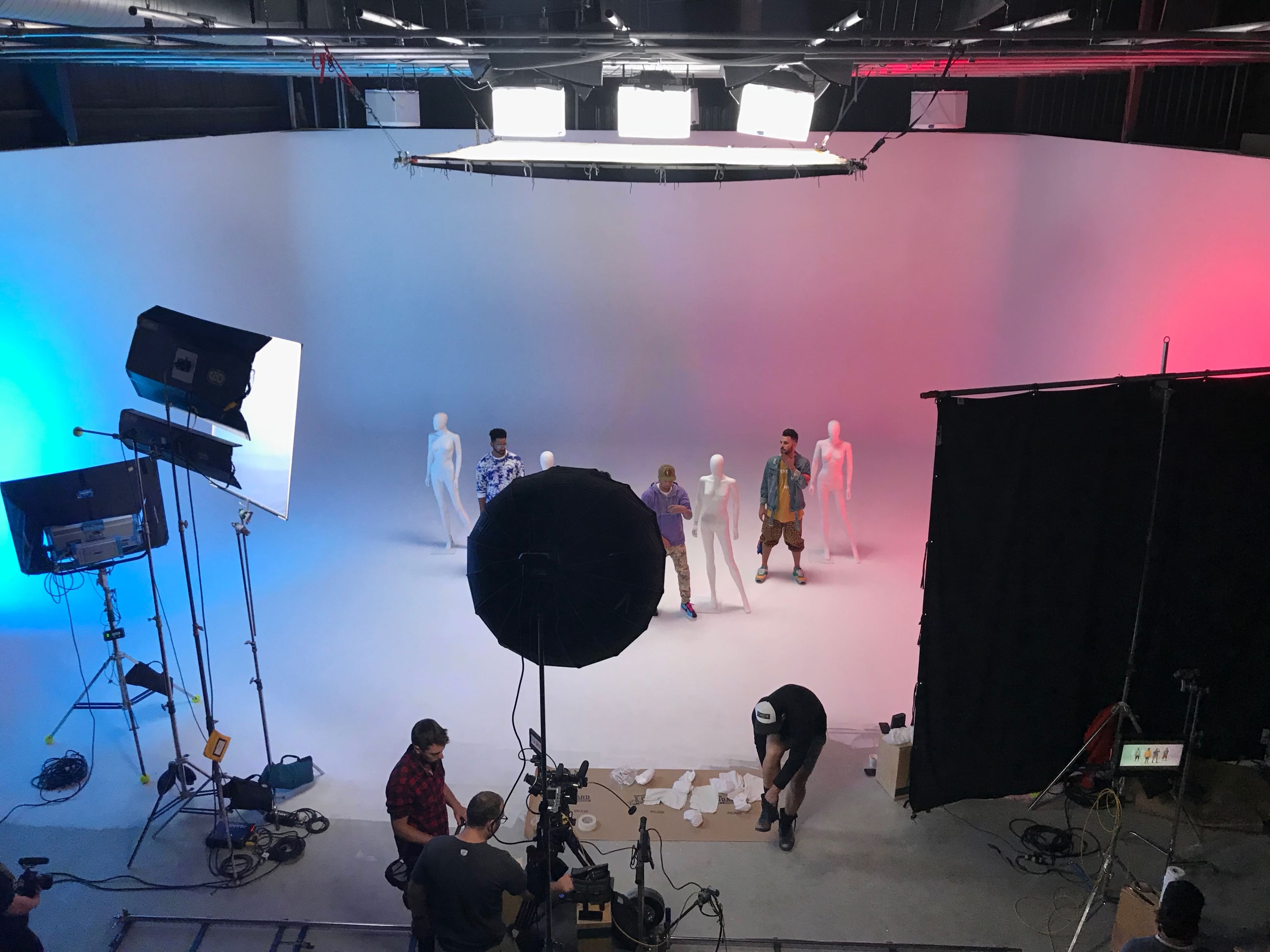 A group of four individuals stands on a stage with white and colored backgrounds, accompanied by several mannequins and studio lighting equipment.
