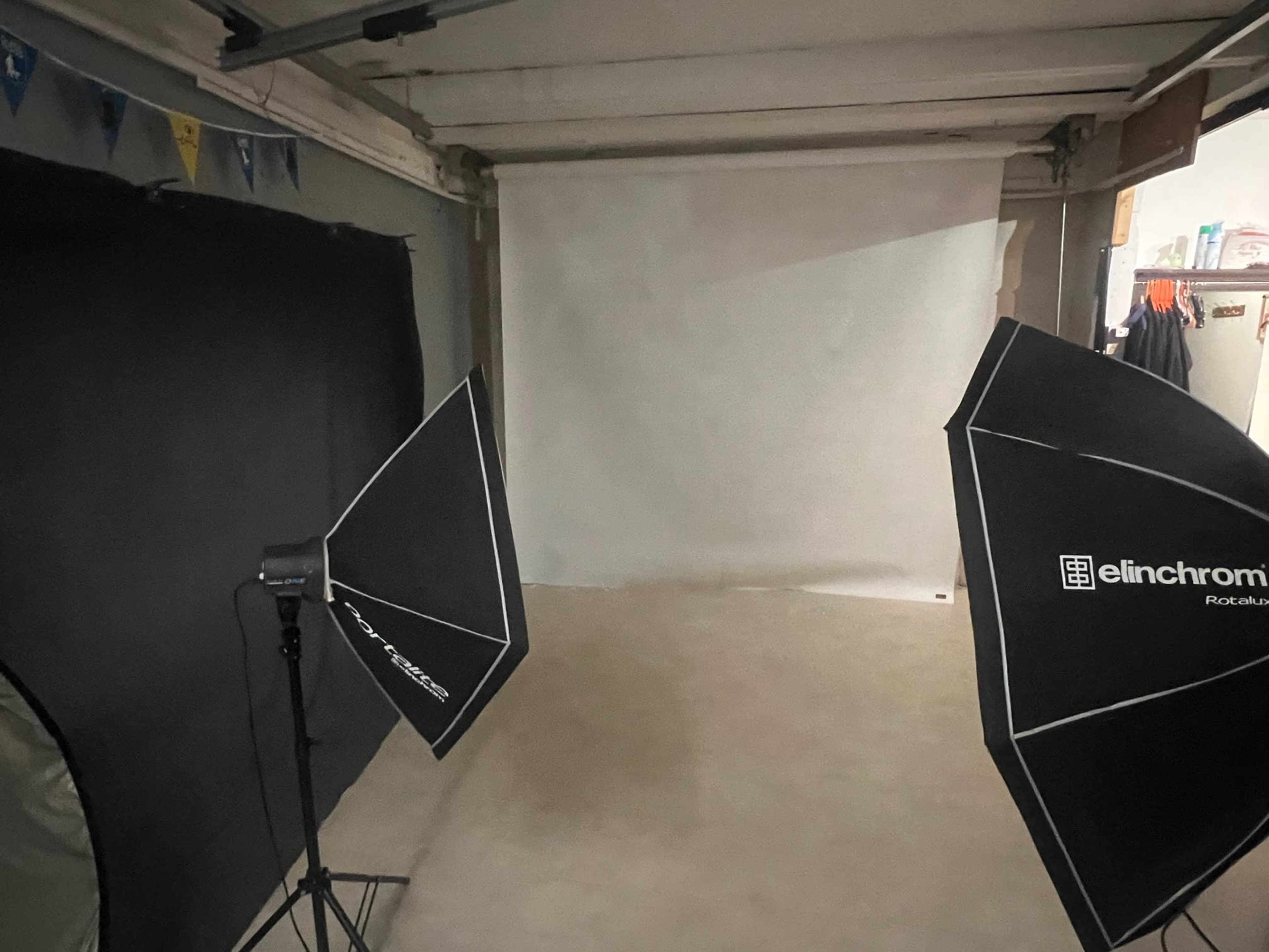 A photography studio setup features two light umbrellas positioned on either side of a blank white backdrop.