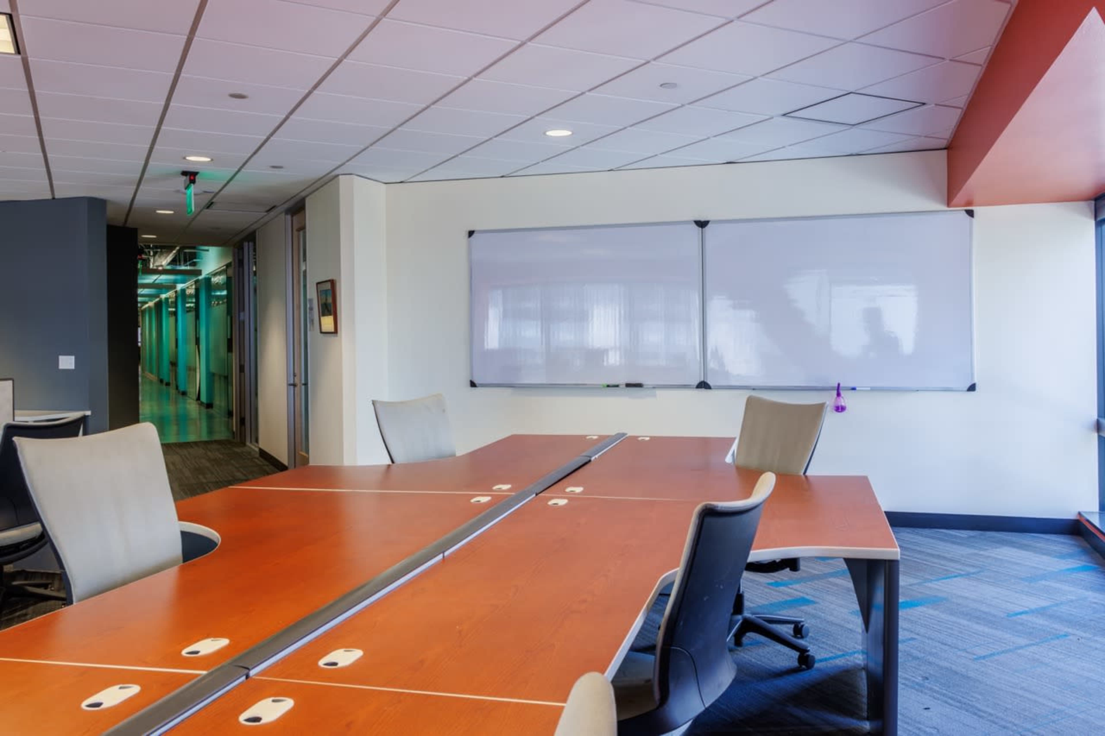 A modern conference room features a large wooden table surrounded by chairs and a whiteboard mounted on the wall.