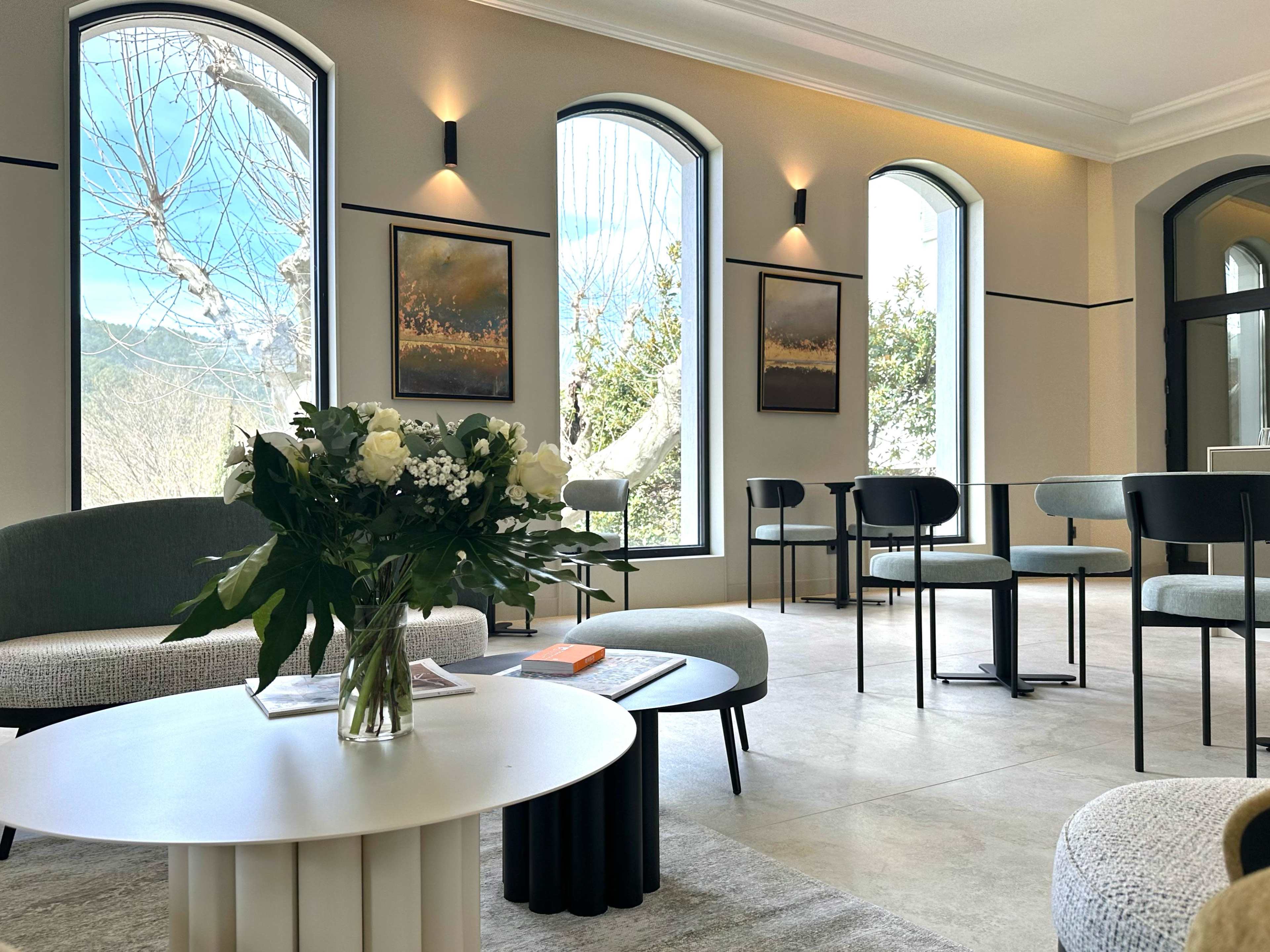 The image shows a modern, stylish room with large arched windows, minimalistic furniture, and elegant decor.