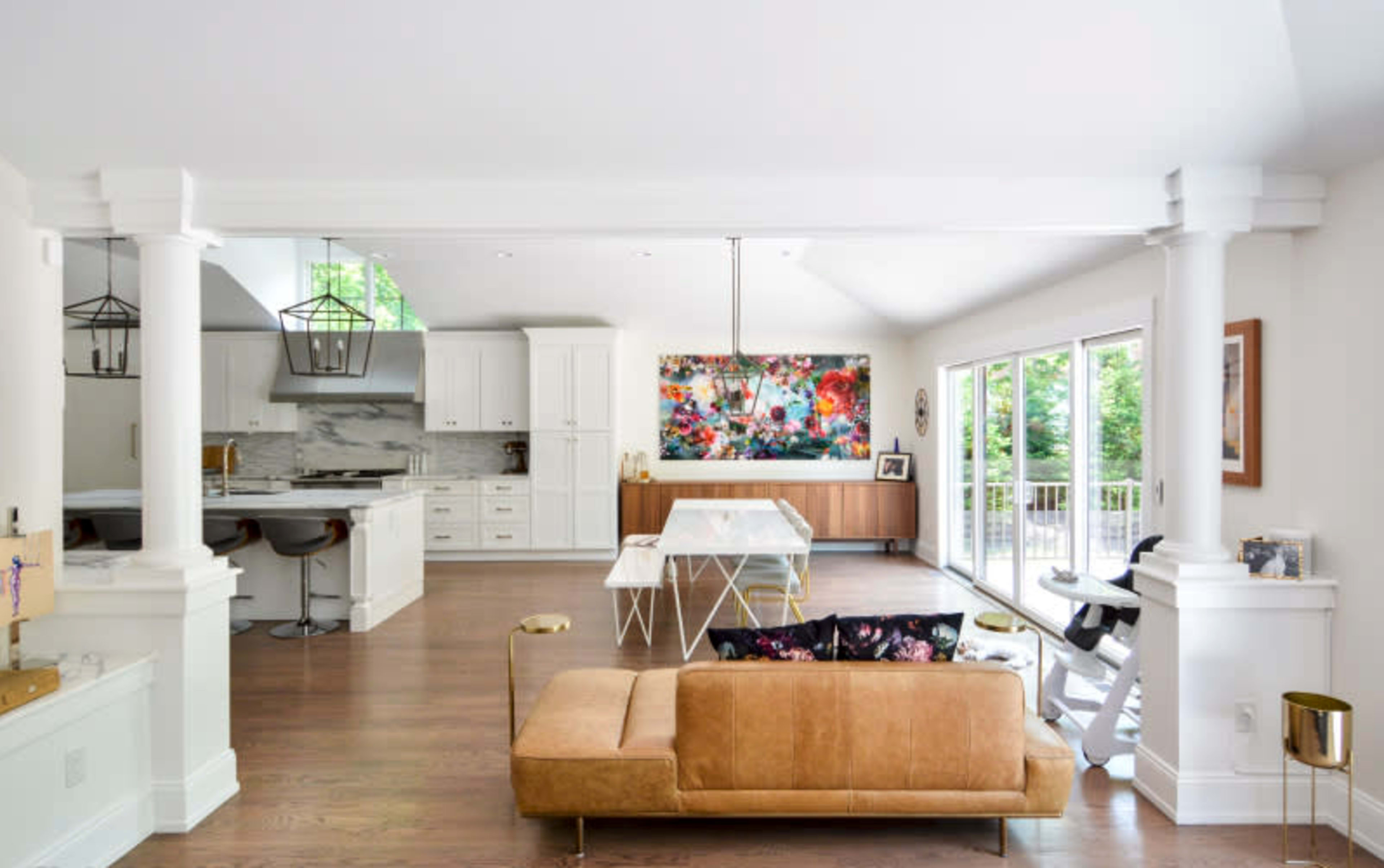 A spacious living area features a brown sofa, a glass dining table, and large windows showcasing greenery outside.