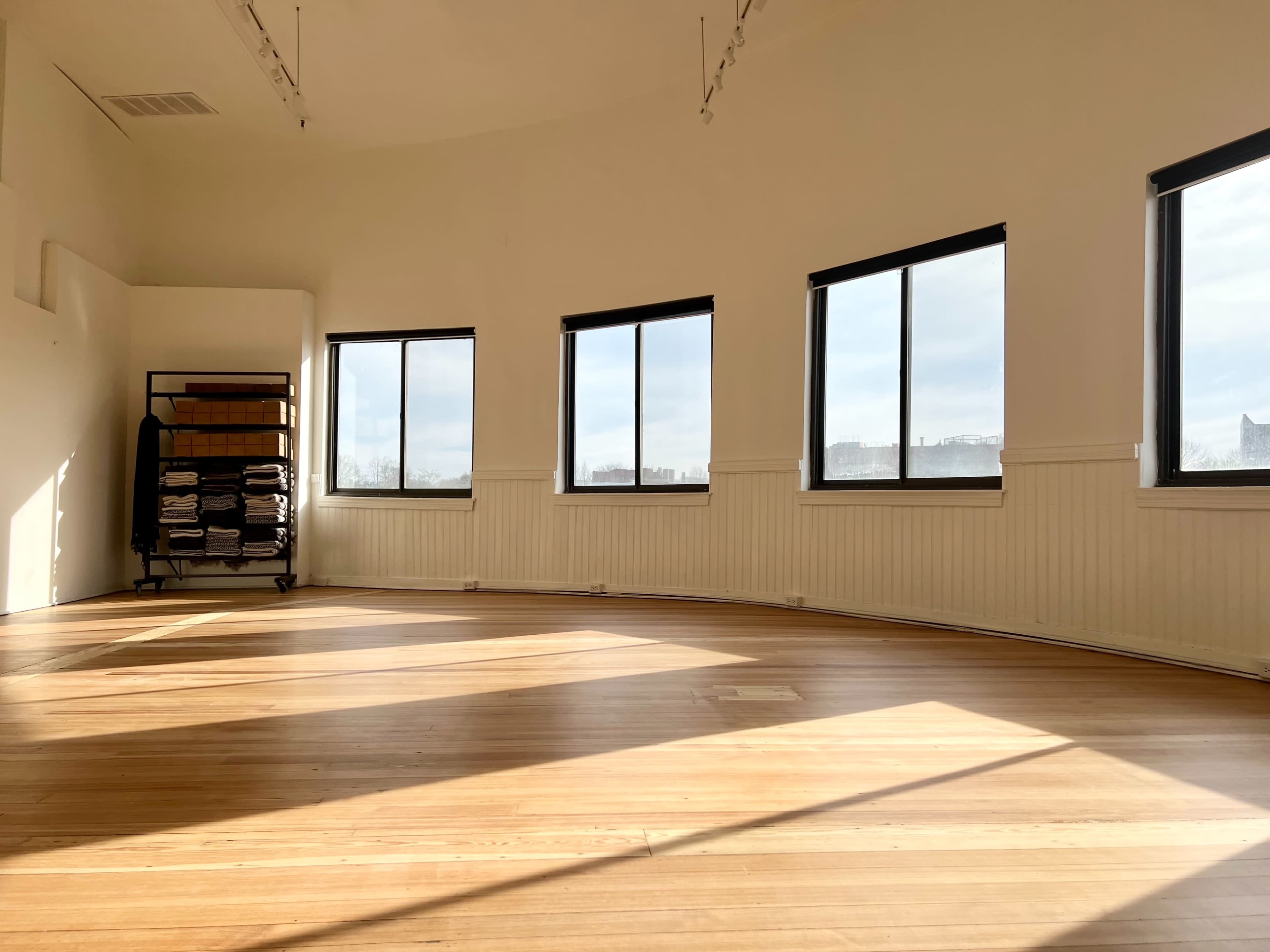 A spacious, well-lit room with wooden flooring and large windows, complemented by a cart of neatly stacked towels in the corner.