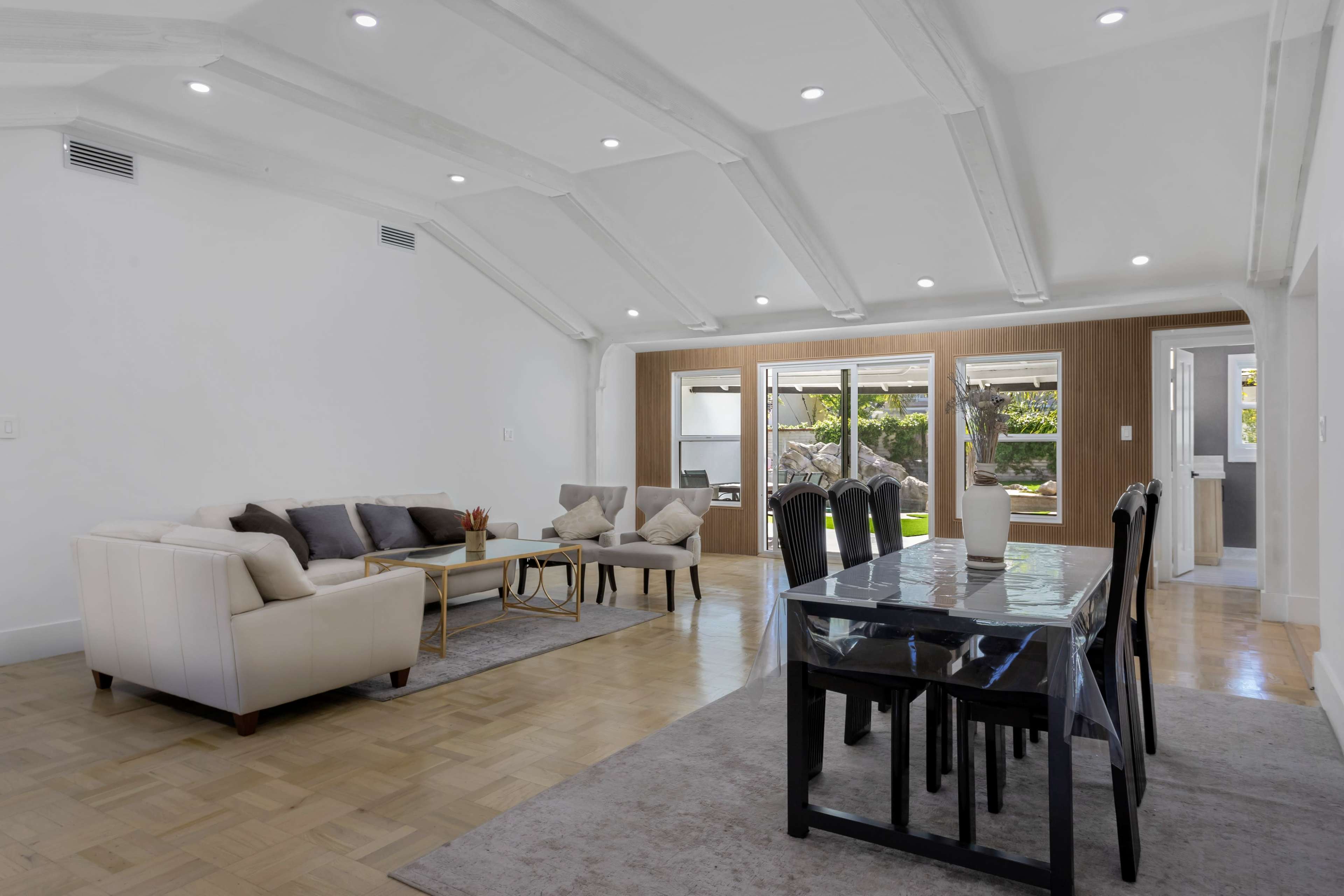 A bright open living and dining area with a modern sofa set, a dining table, and large windows overlooking a garden.