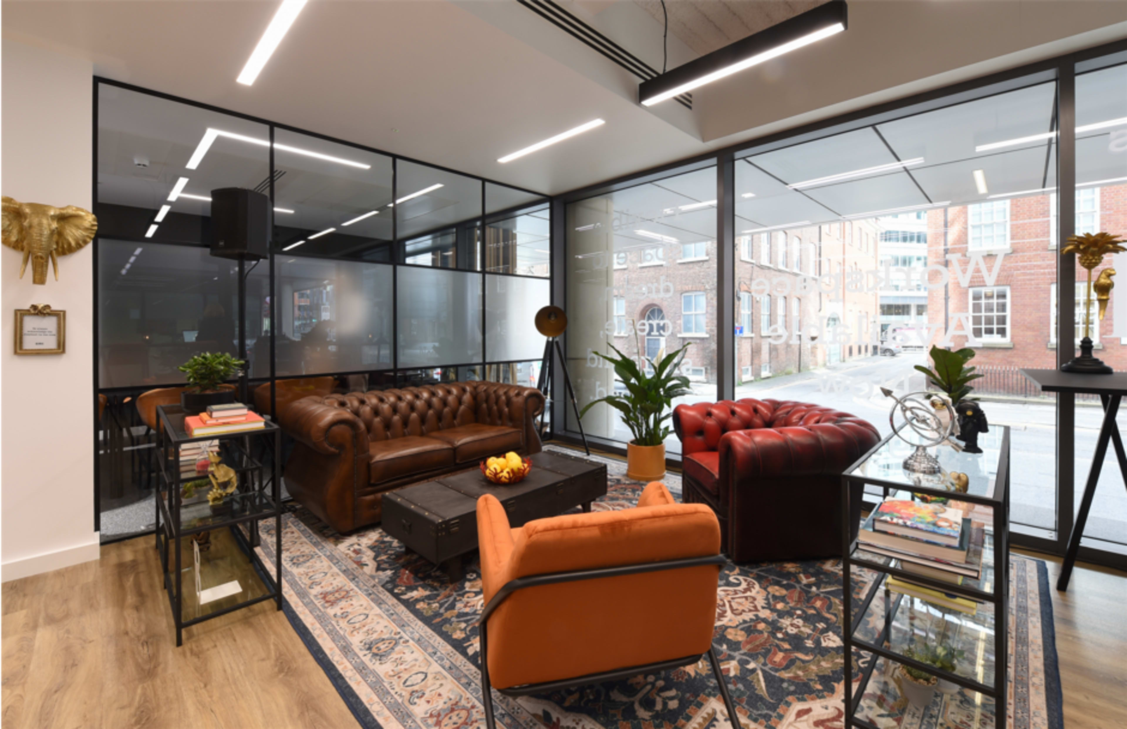 A modern lounge area with two leather sofas, a coffee table, and large windows revealing a street view.