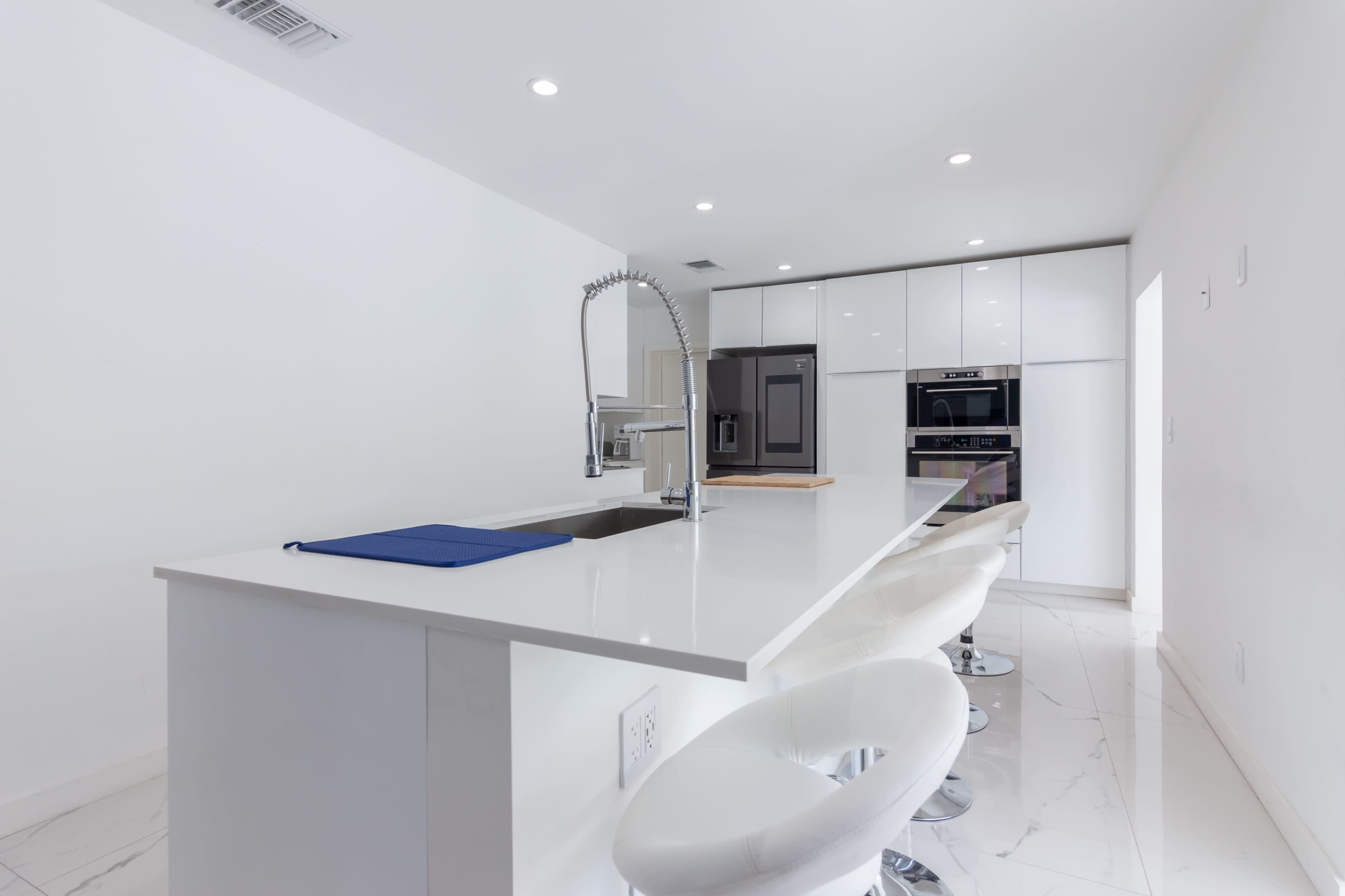 A modern kitchen featuring a white countertop with a sink and bar stools, along with sleek cabinets and built-in appliances.
