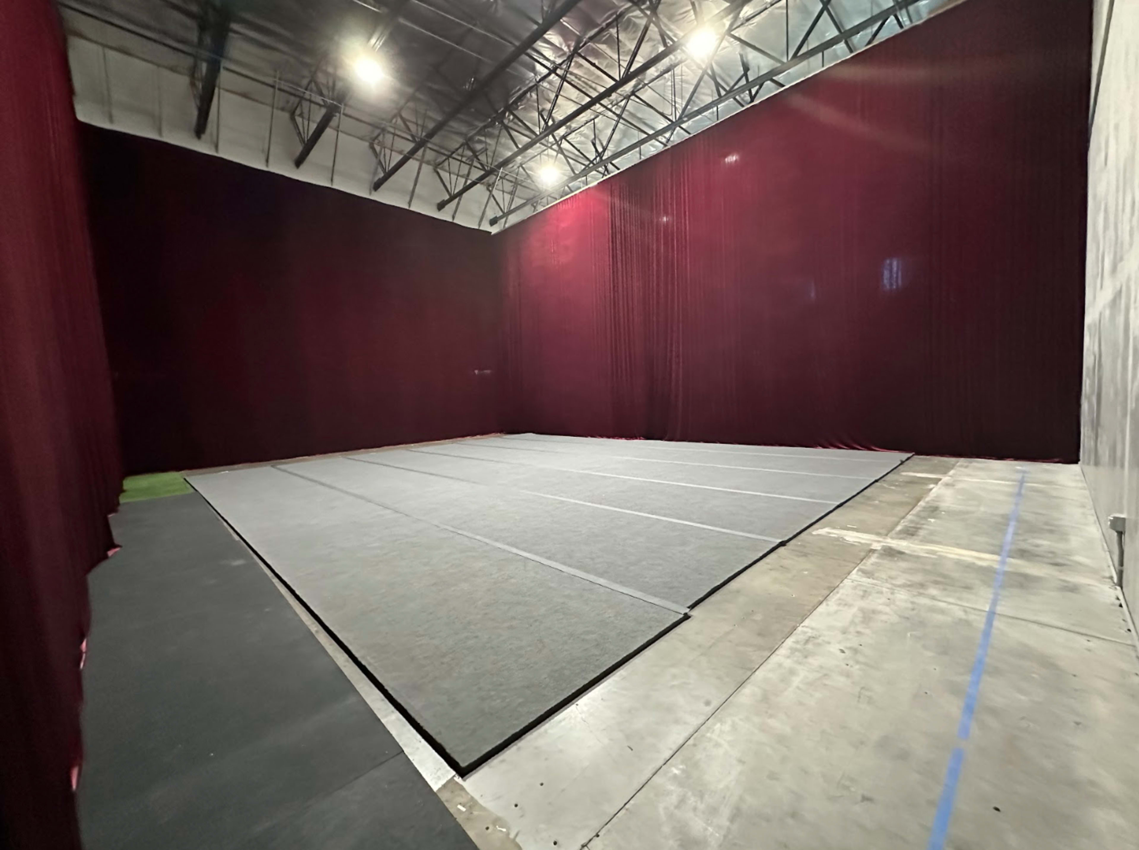 A large, empty room with dark red curtains lining the walls and a gray mat laid out on the floor.