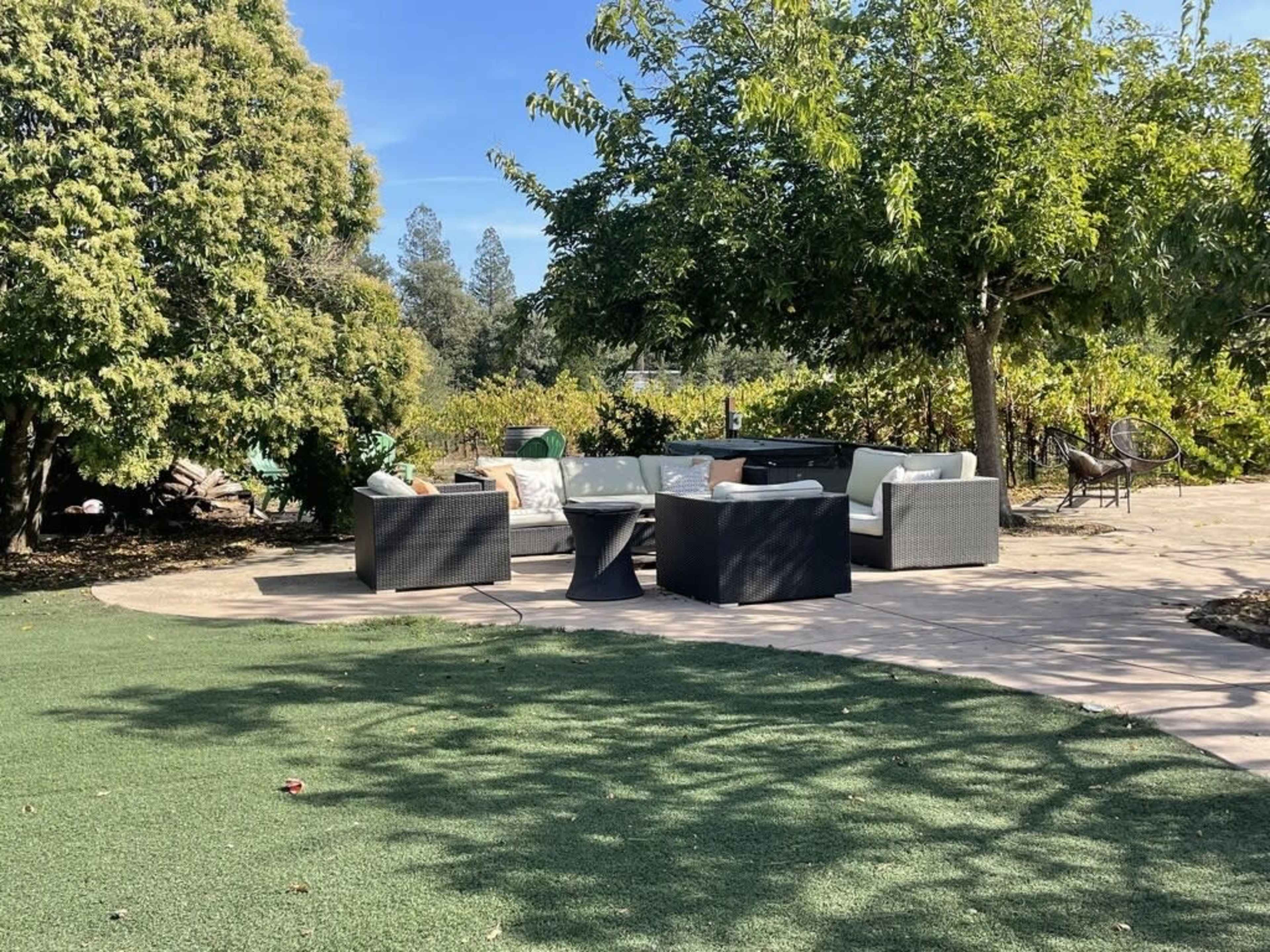A patio area features a seating arrangement with four chairs and a table, surrounded by greenery and trees.