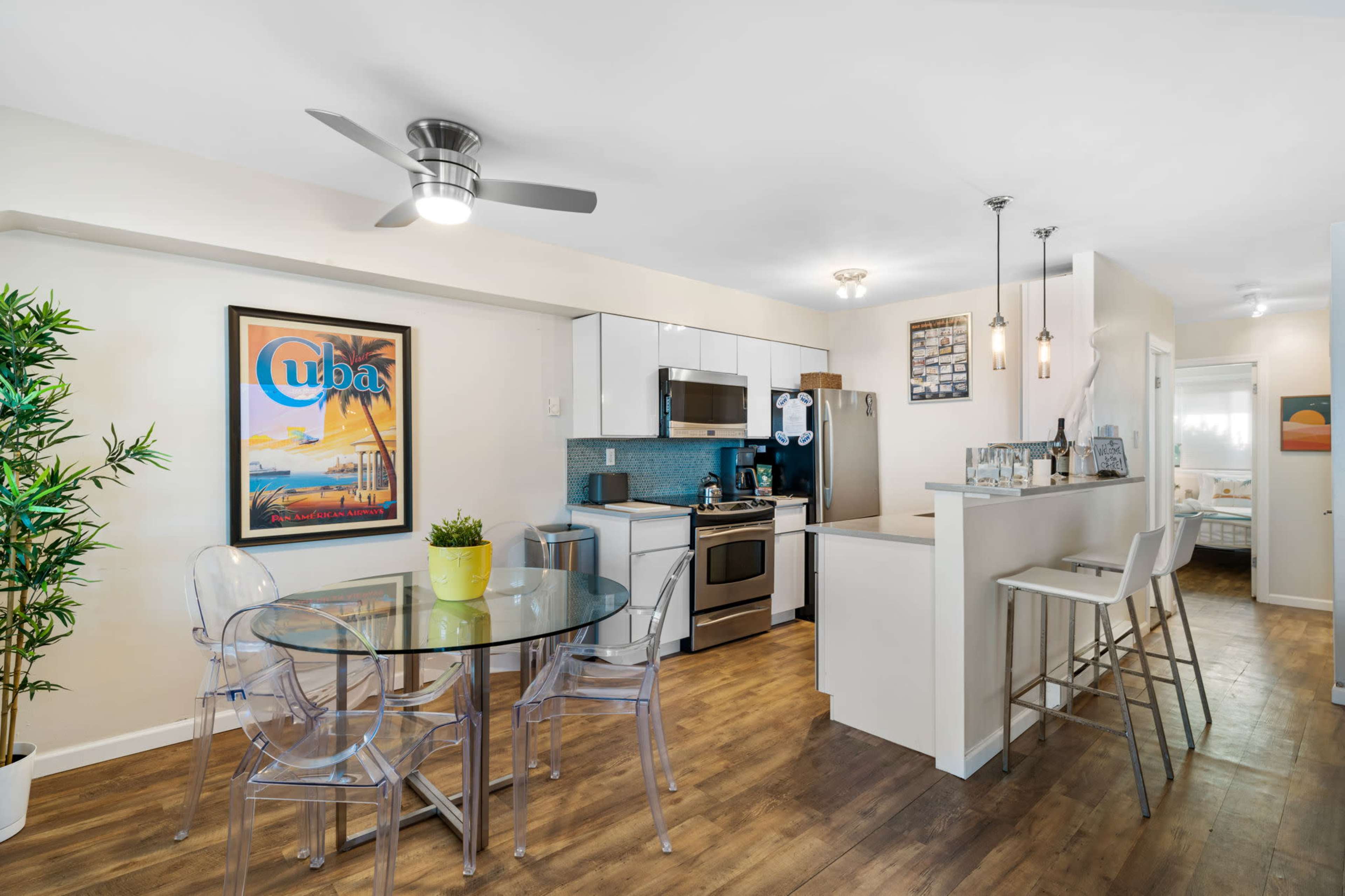 A modern kitchen and dining area featuring a round glass table, clear chairs, and stainless steel appliances.