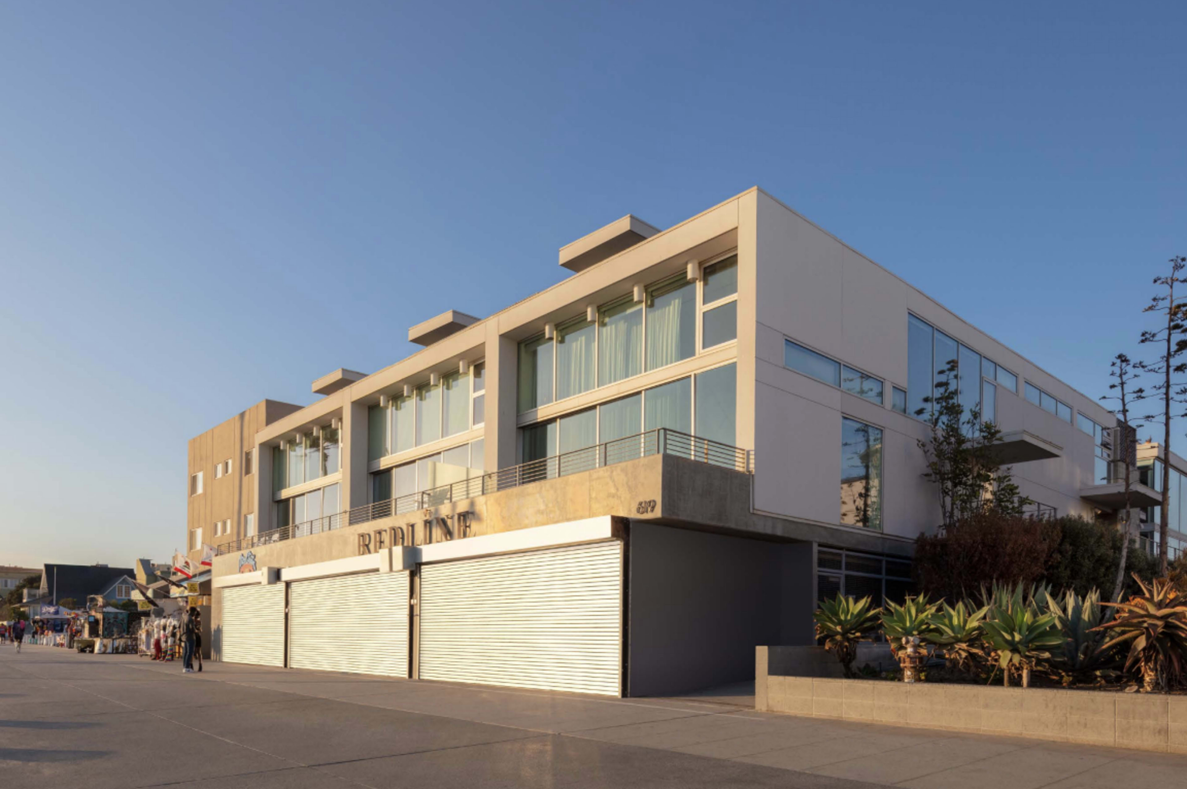 The image shows a modern building with large windows, located along a walkway, and featuring a roll-up door in front.