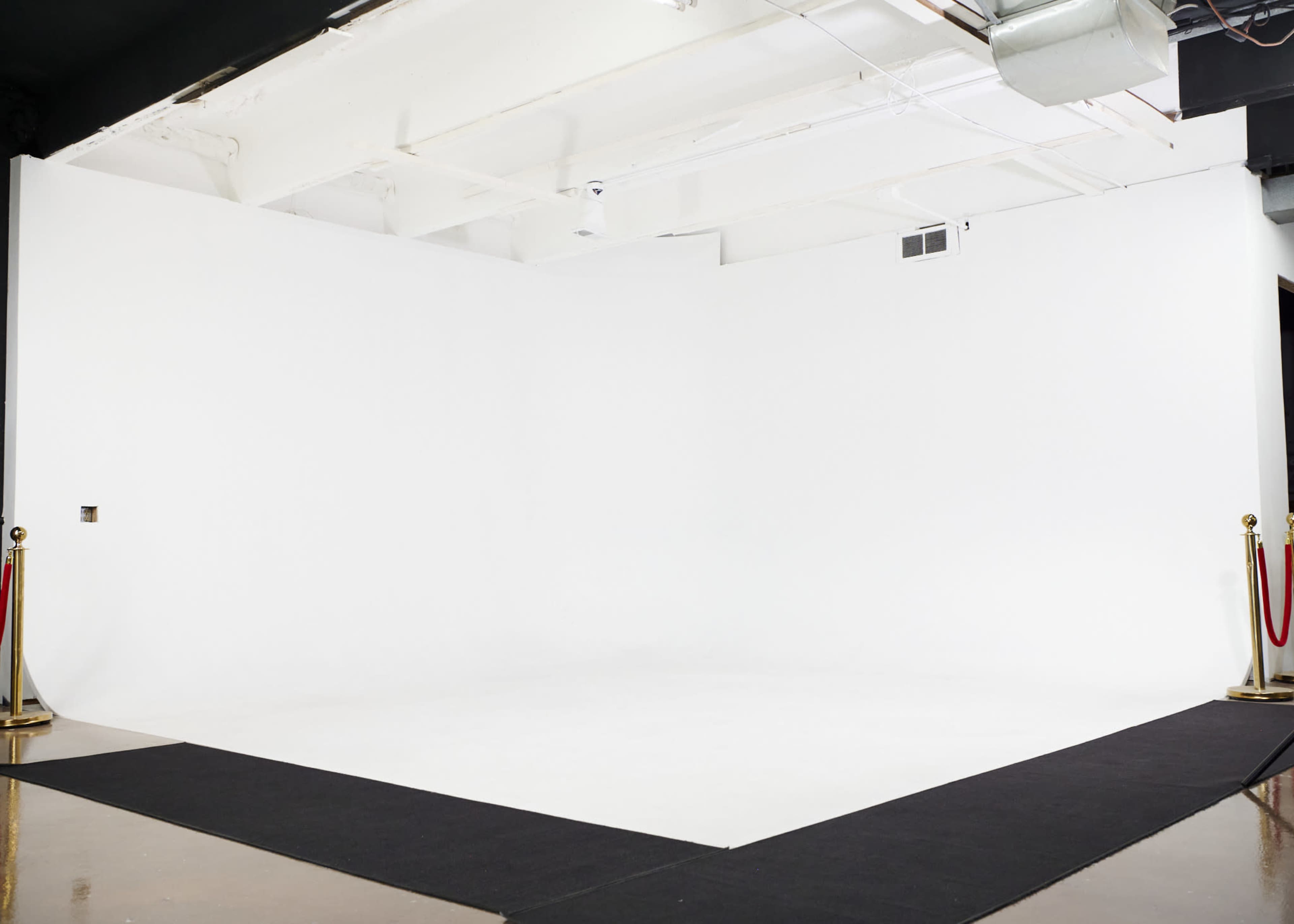 The image shows a spacious, empty studio with a white backdrop and black flooring.