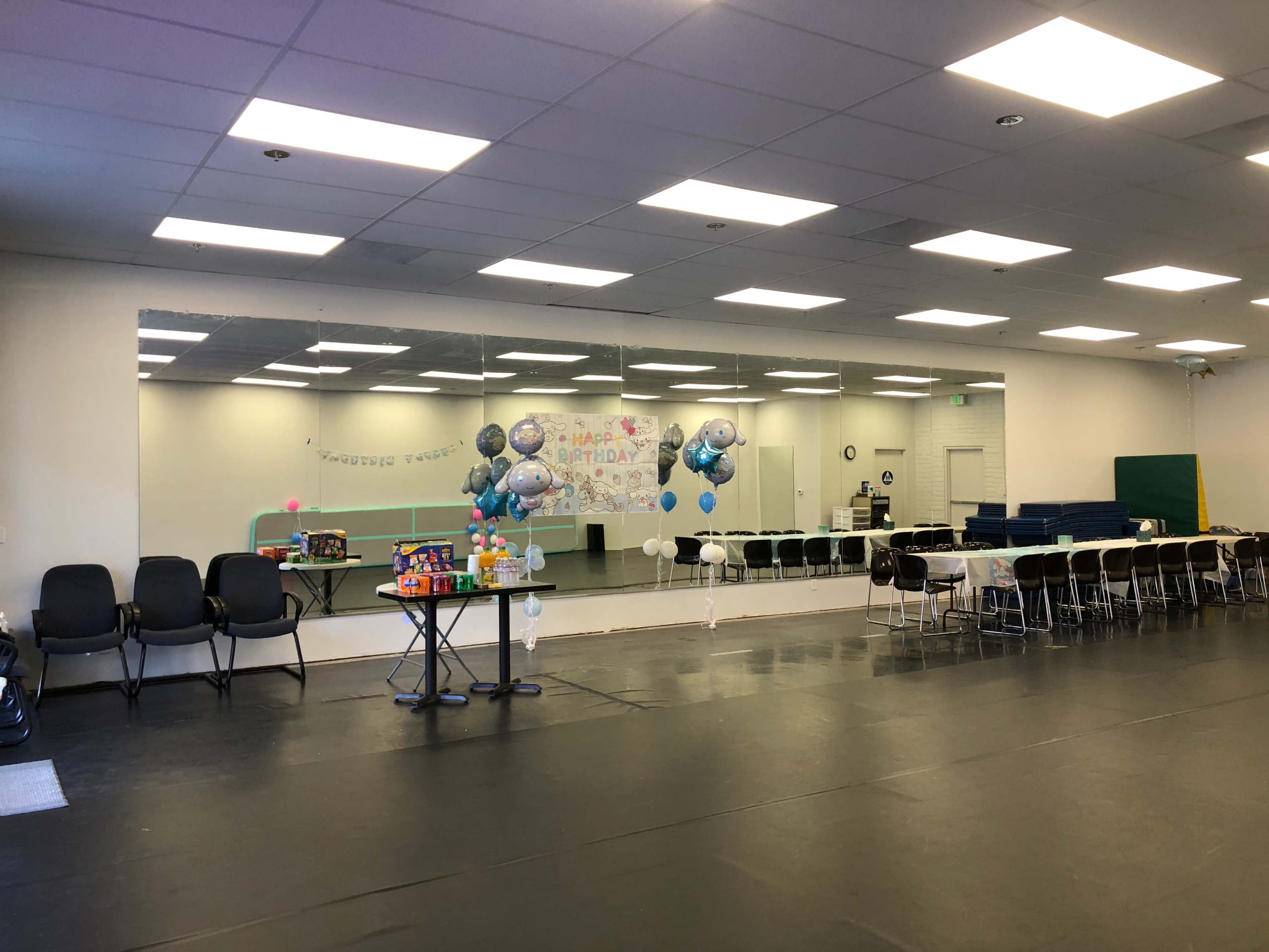 The image shows a spacious indoor party area with a mirrored wall, colorful decorations, balloons, and seating arranged around tables.