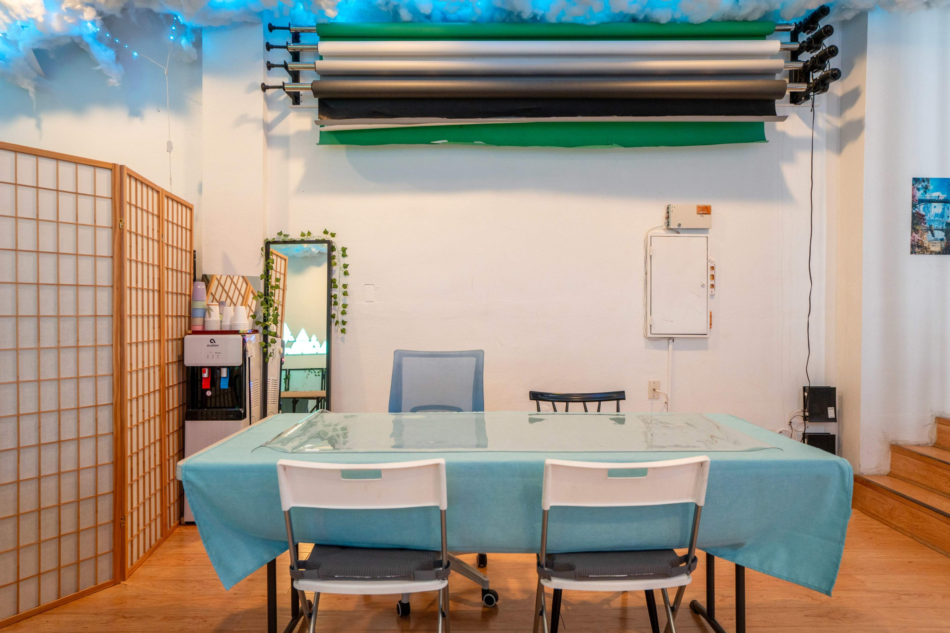 A table covered with a turquoise cloth is set in a room with a folding screen, a mirror, and background rolls mounted on the wall.