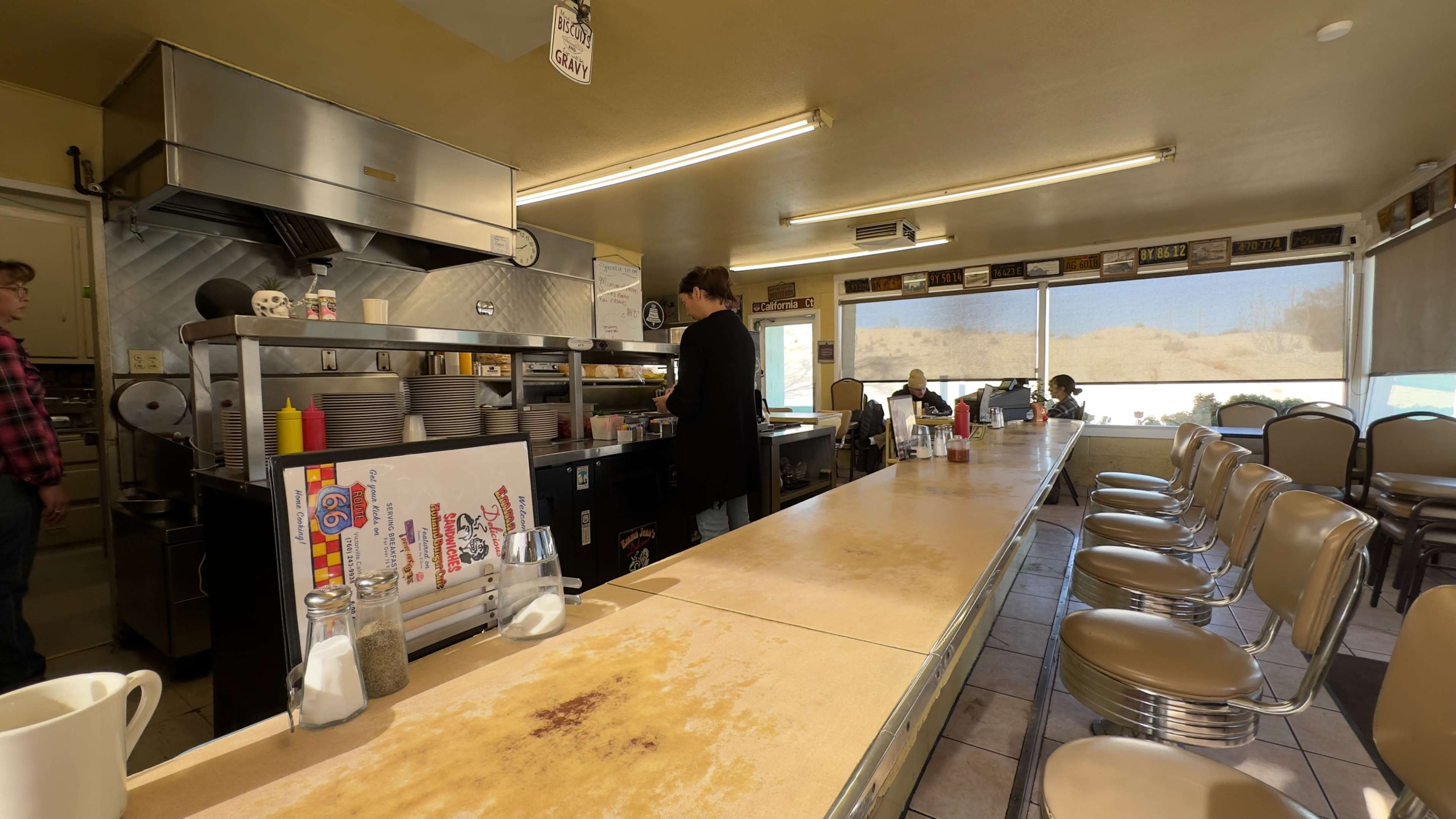 The image shows the interior of a diner with a long counter, kitchen area in the back, and several patrons seated by large windows.