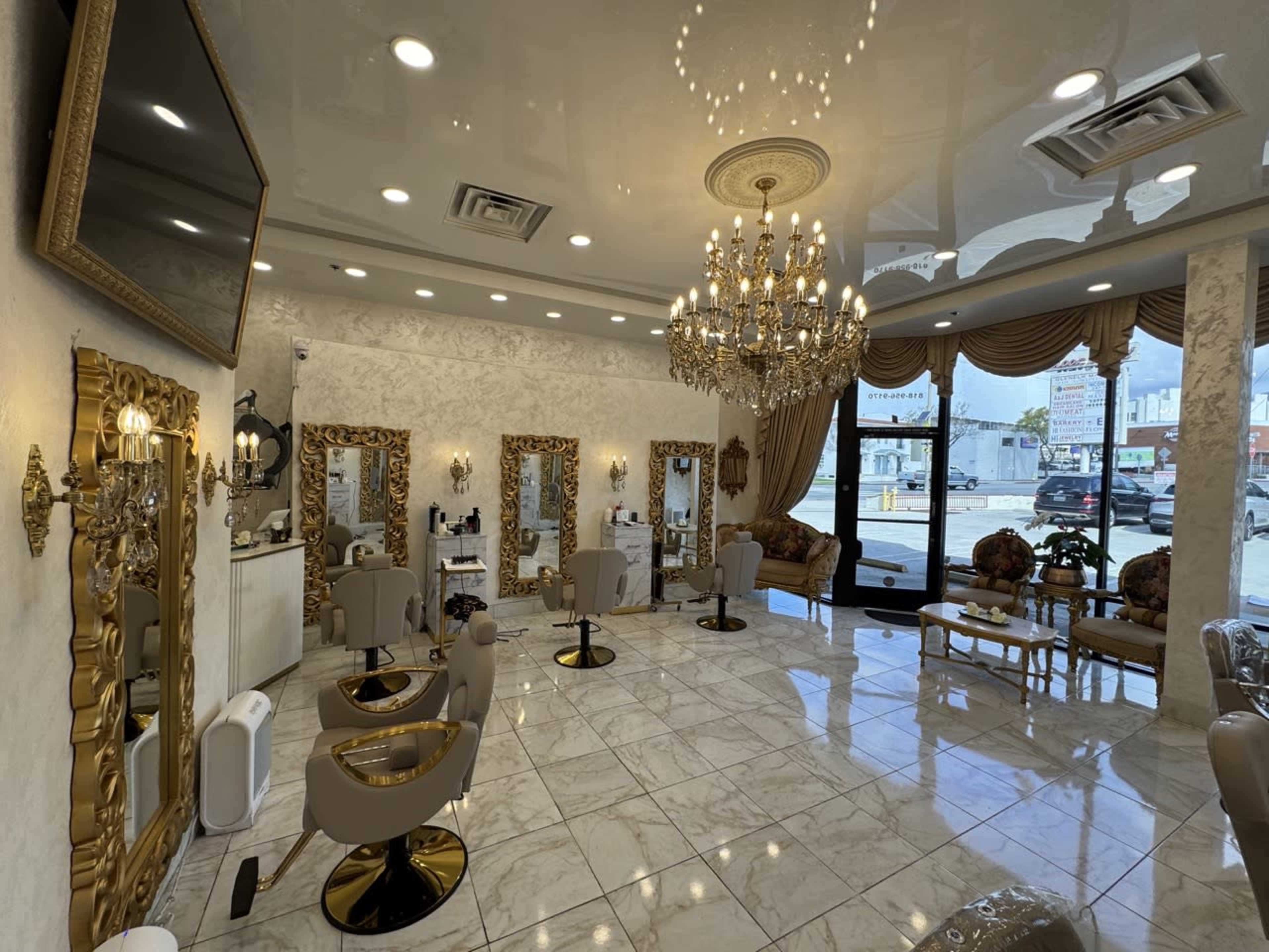 The image shows a stylish hair salon with elegant decor, featuring golden mirrors, chandeliers, and multiple salon chairs arranged in a spacious, well-lit area.