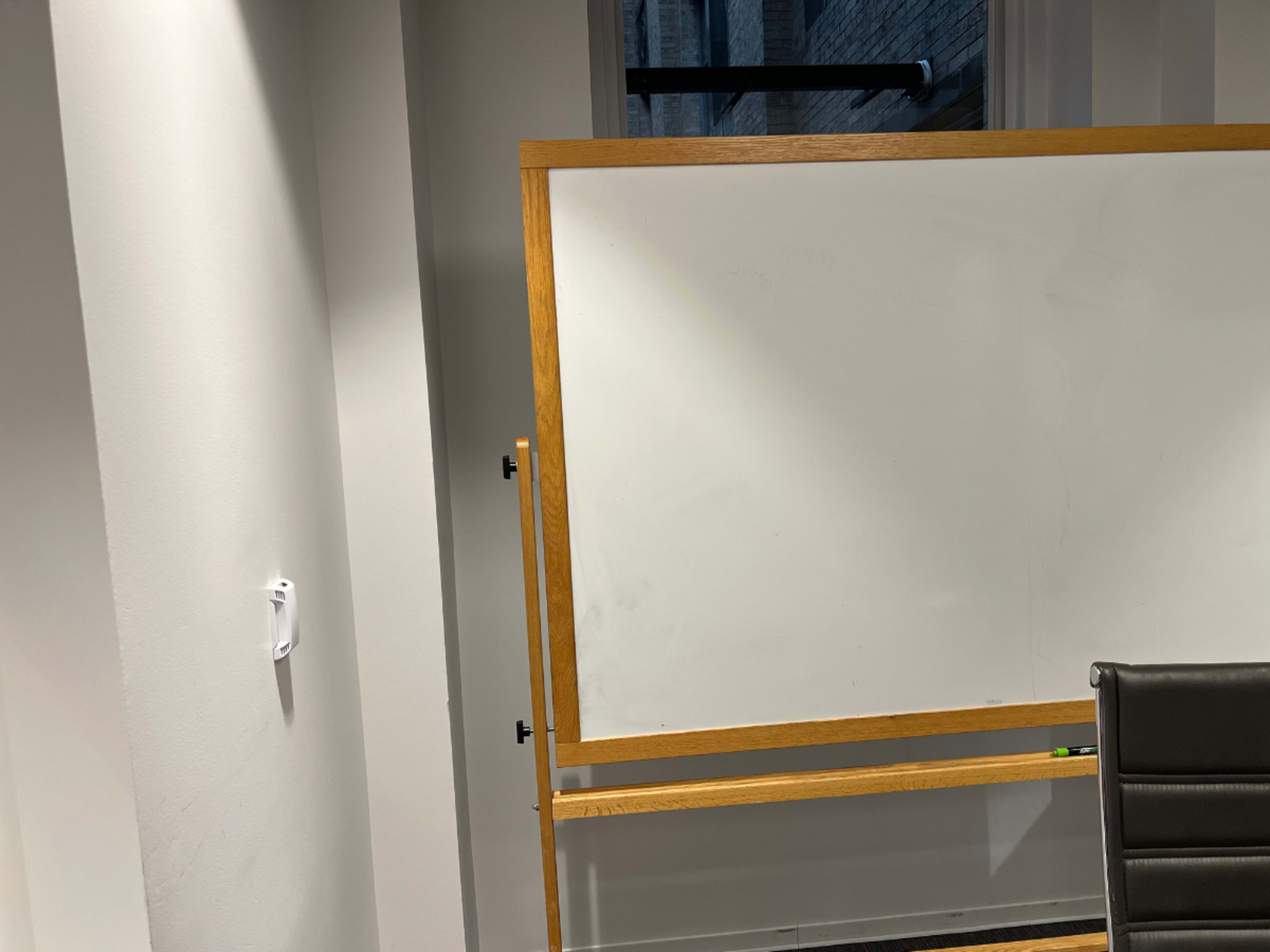 An empty whiteboard mounted in a well-lit room, adjacent to a black office chair.