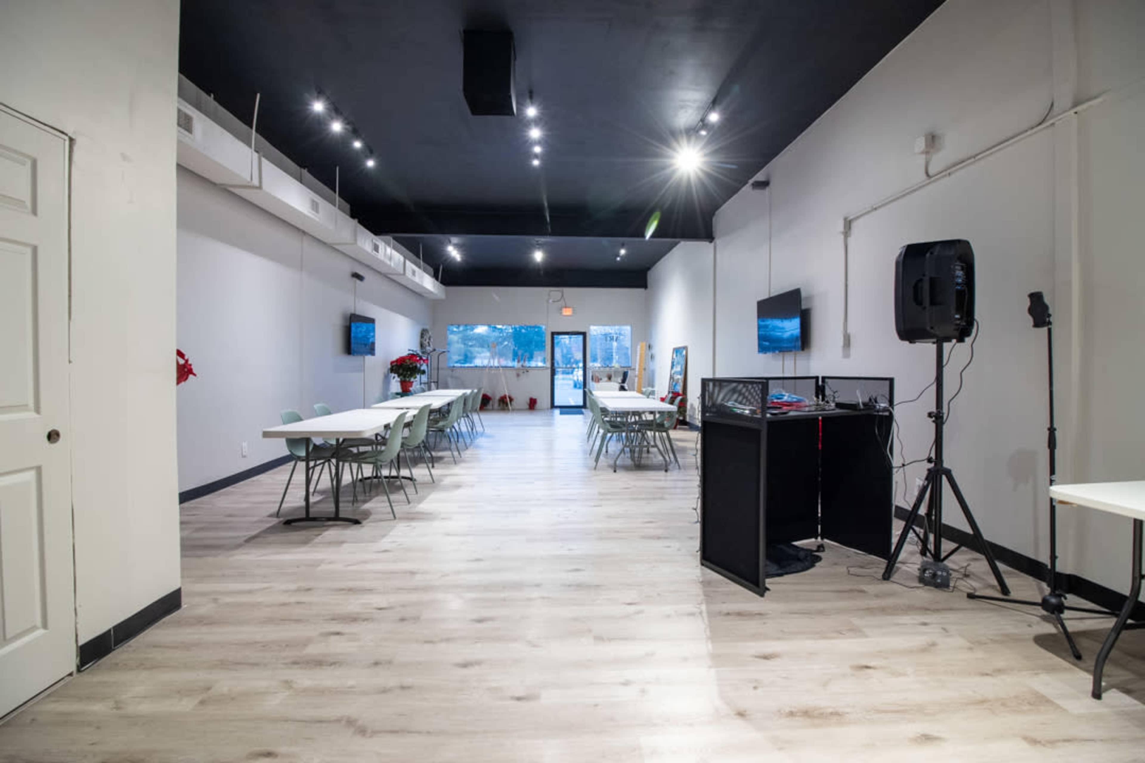 A spacious, well-lit event room with several tables arranged in a symmetrical layout and a sound system in the corner.