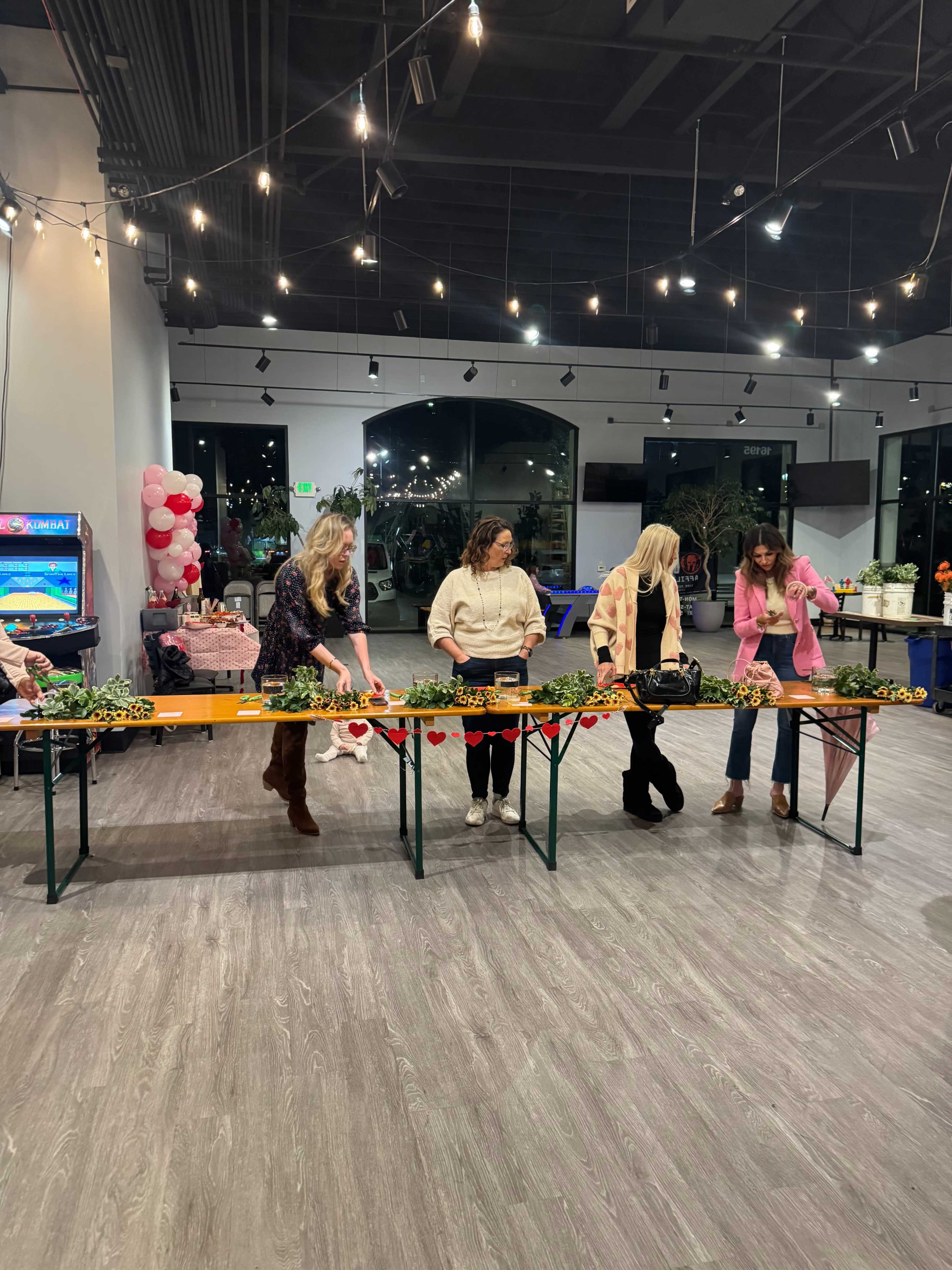 A group of five women are engaged in an activity at a decorated indoor space with string lights and festive decorations.