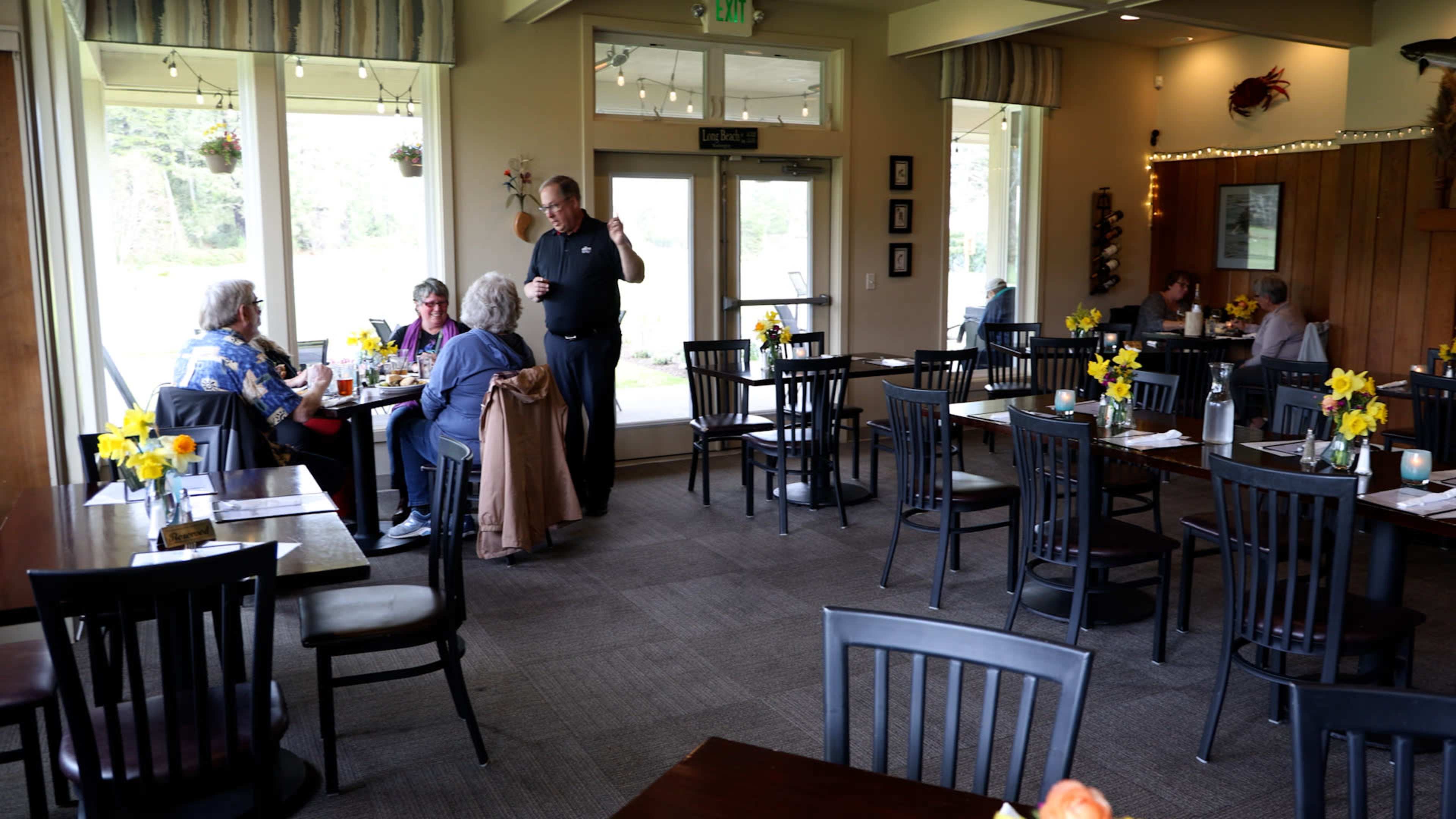 A waitress takes an order from a group of diners seated at a table in a restaurant with yellow flowers on each table.