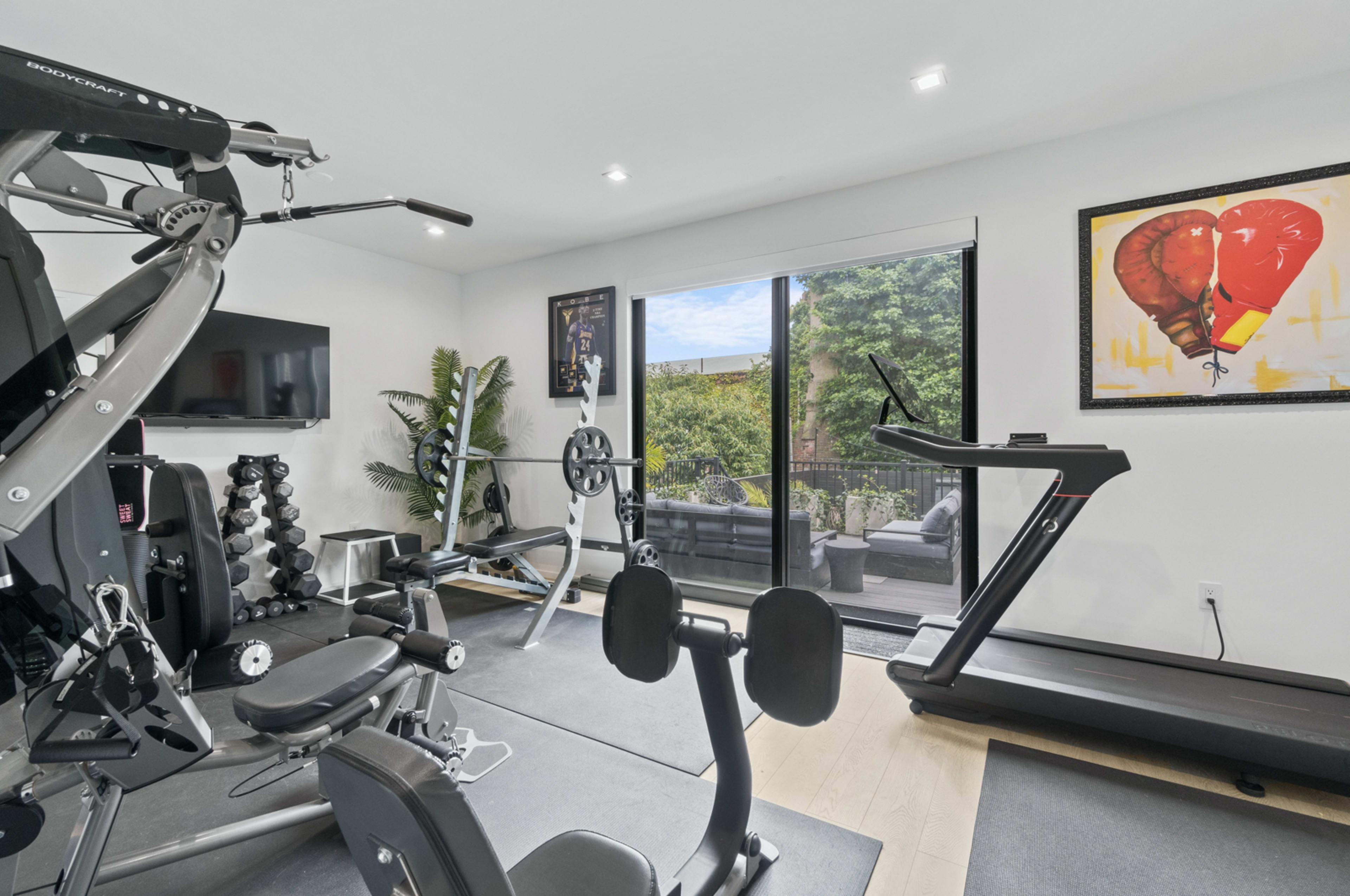 A home gym equipped with exercise machines, free weights, and a large window with a view of an outdoor patio.