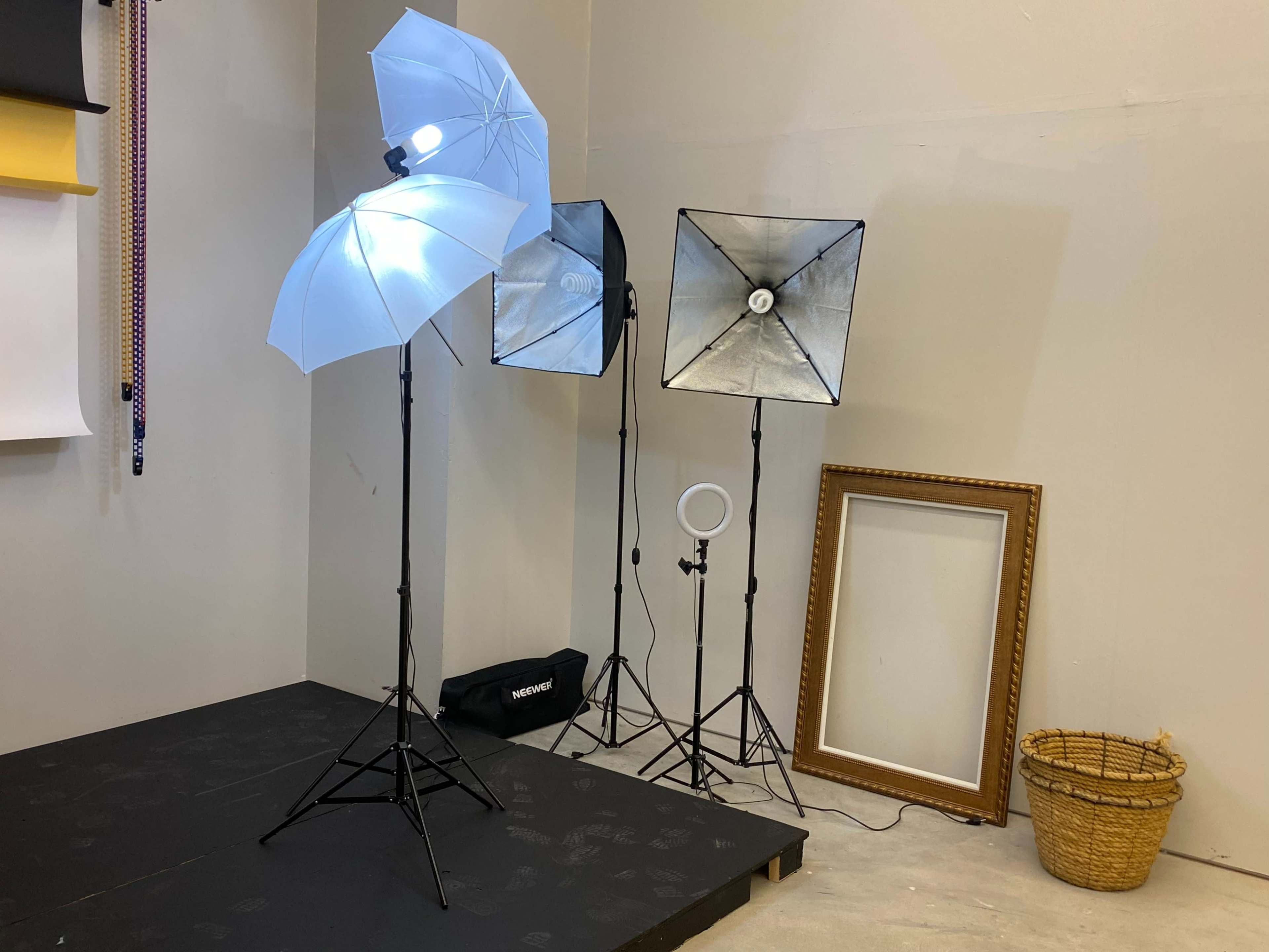 A photography setup is shown with multiple light sources, including umbrellas and softboxes, alongside a blank frame and a basket.