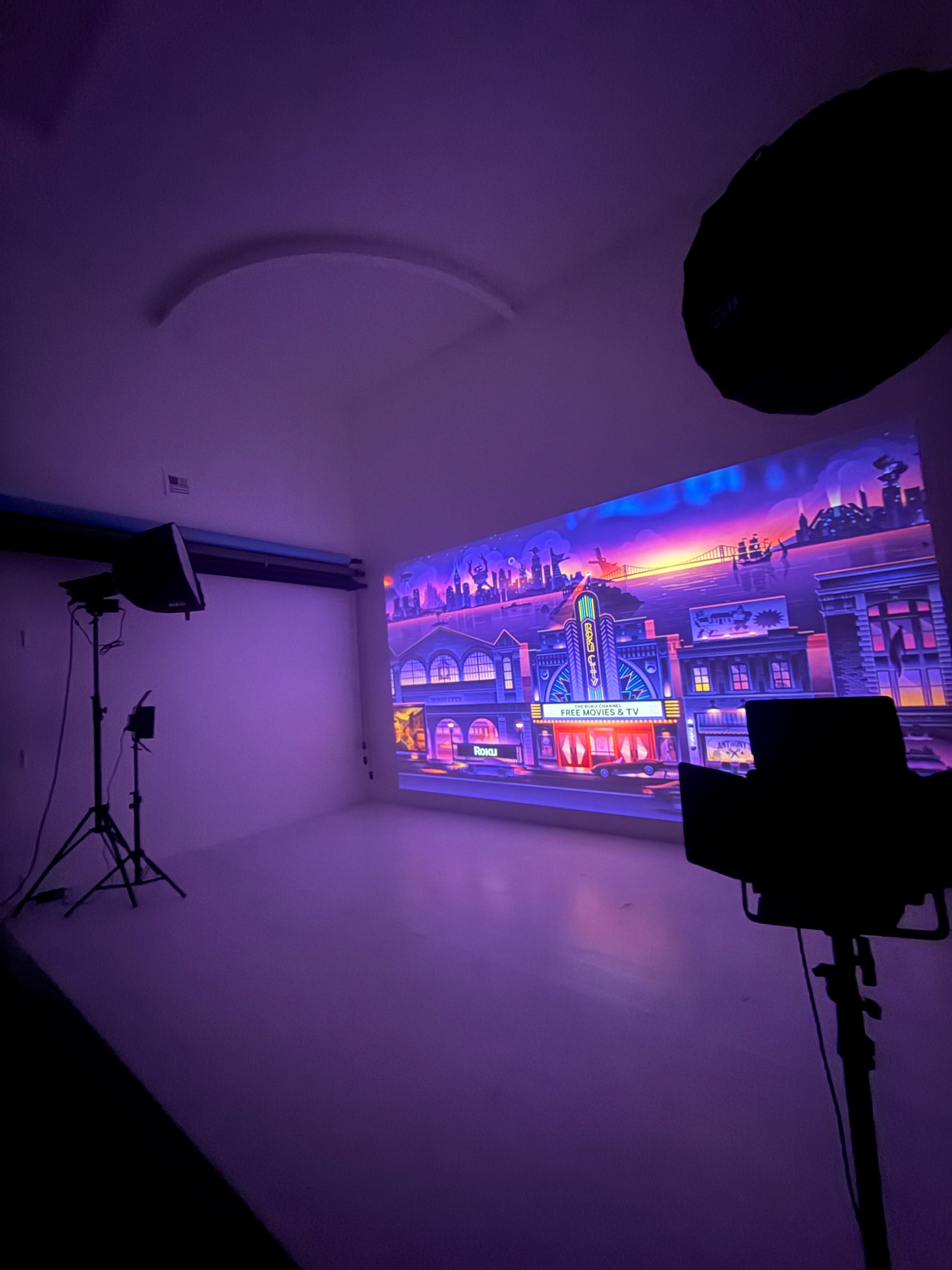 The image shows a photography studio with a brightly lit backdrop depicting a colorful street scene.
