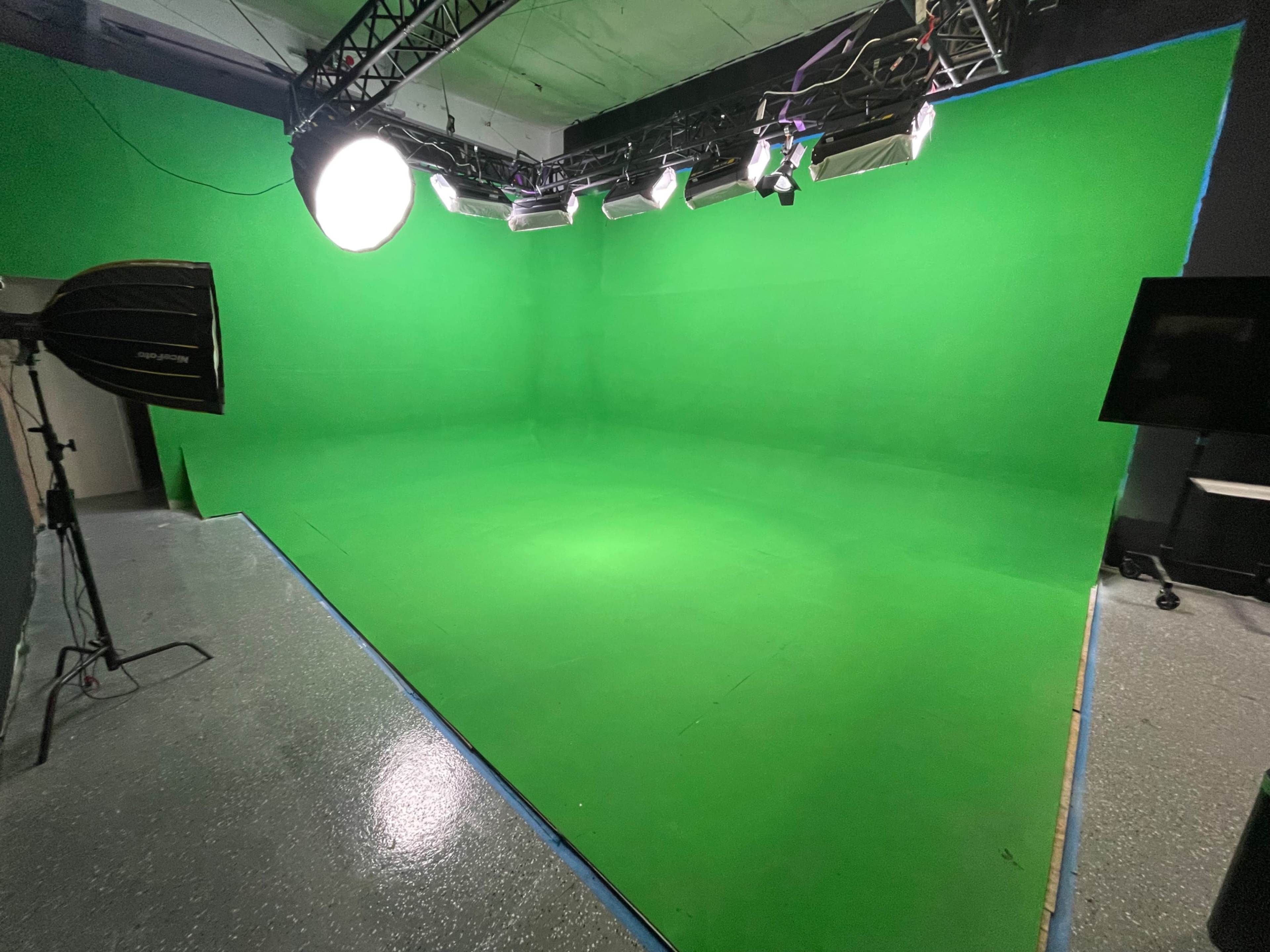 The image shows a green screen studio with multiple lights and equipment set up for video production.
