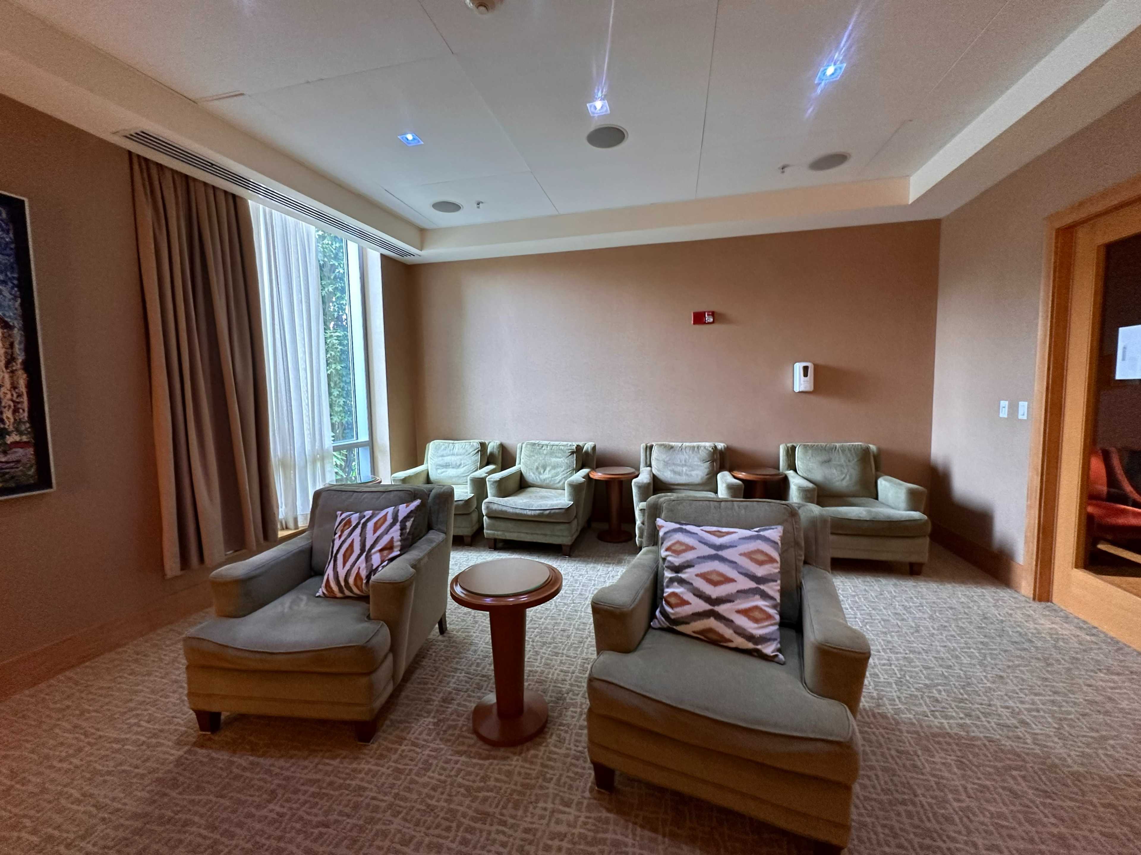 The image shows a well-lit lounge area featuring several green upholstered chairs with decorative pillows around a small round table.