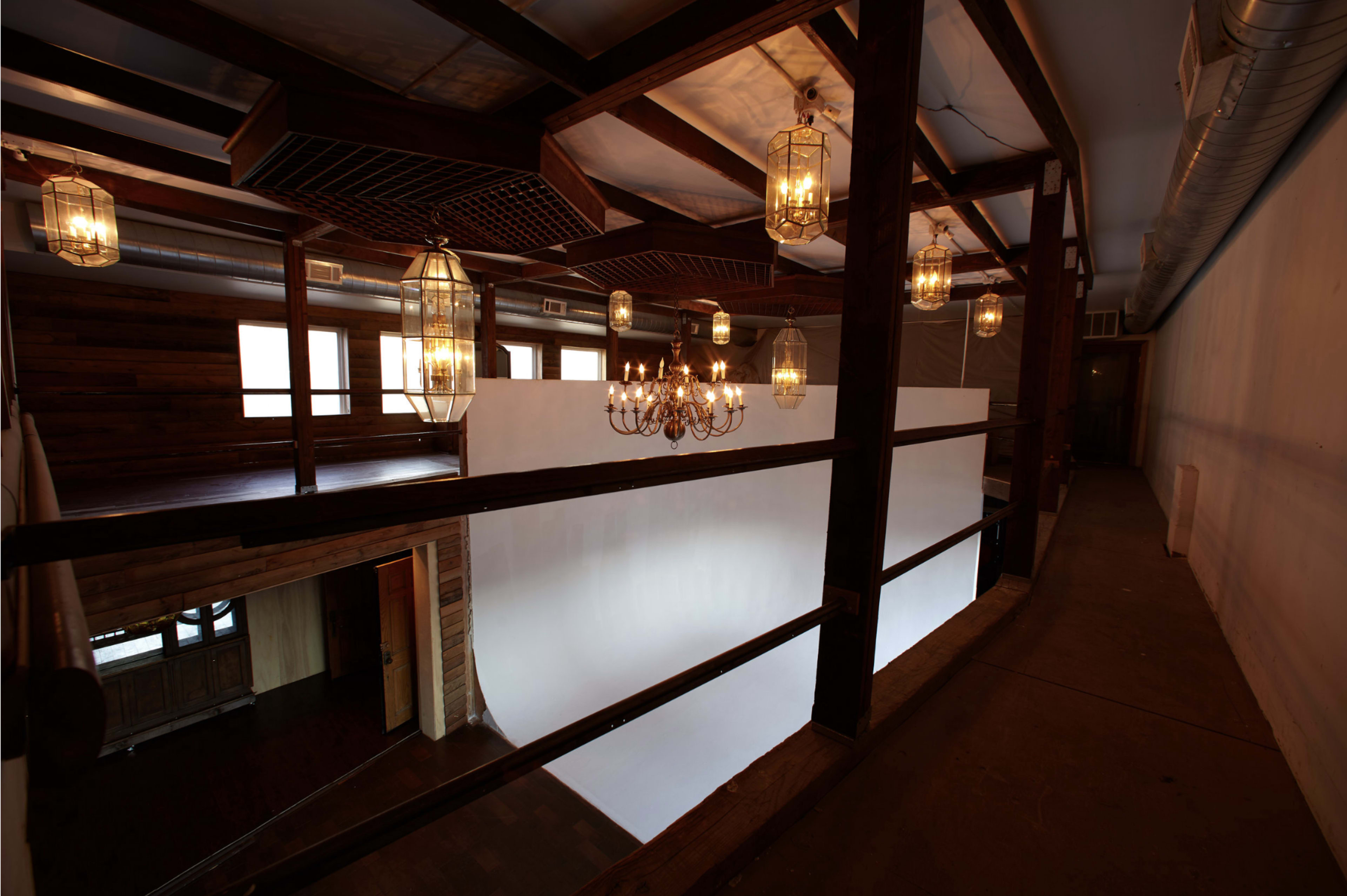 A spacious indoor area with a high ceiling, featuring a white backdrop, wooden beams, and multiple hanging light fixtures.