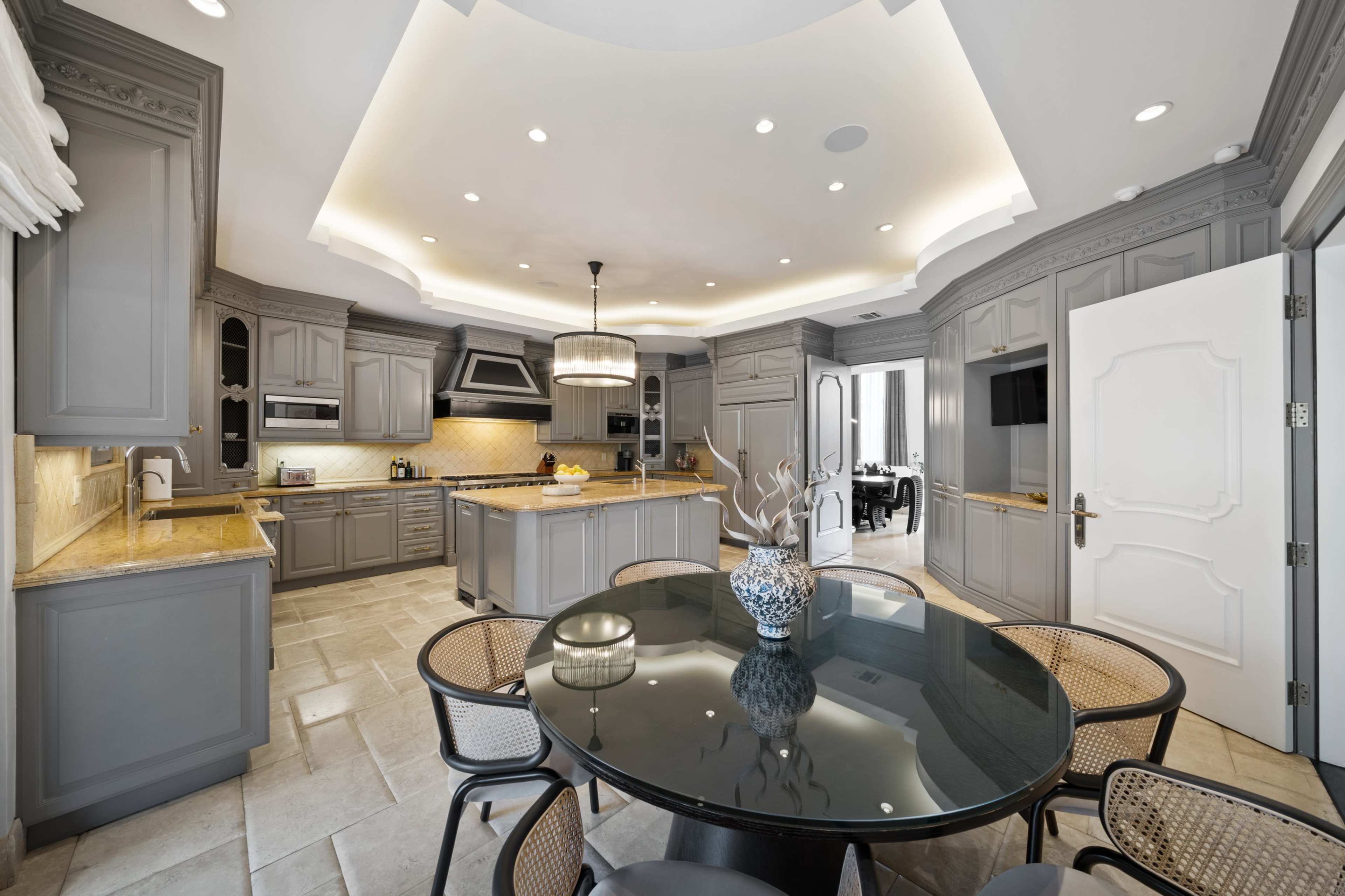 The kitchen features gray cabinets, a dark circular dining table, and a large island with golden countertops.