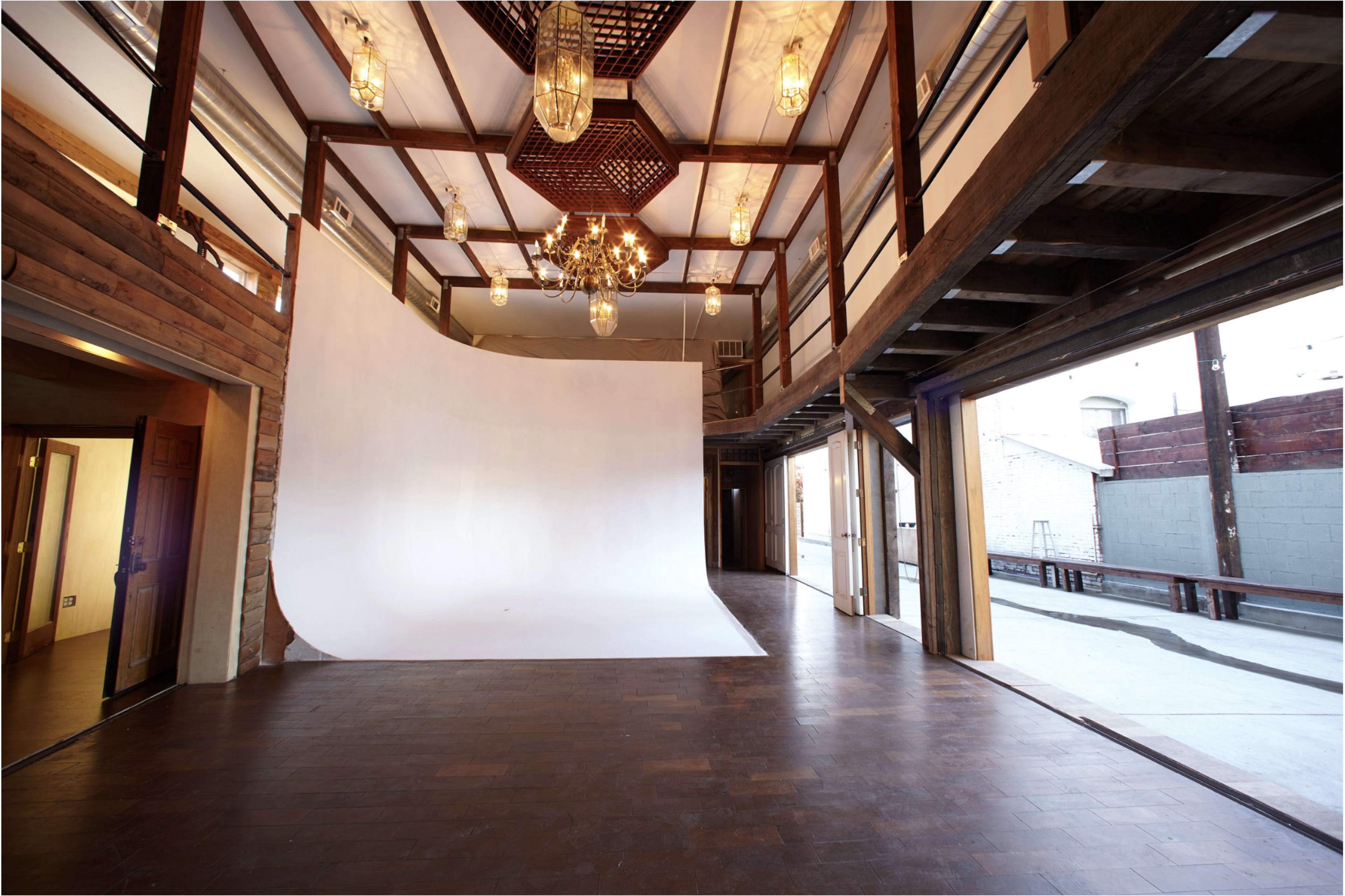 A spacious photography studio with a white backdrop, wooden beams, and hanging light fixtures.