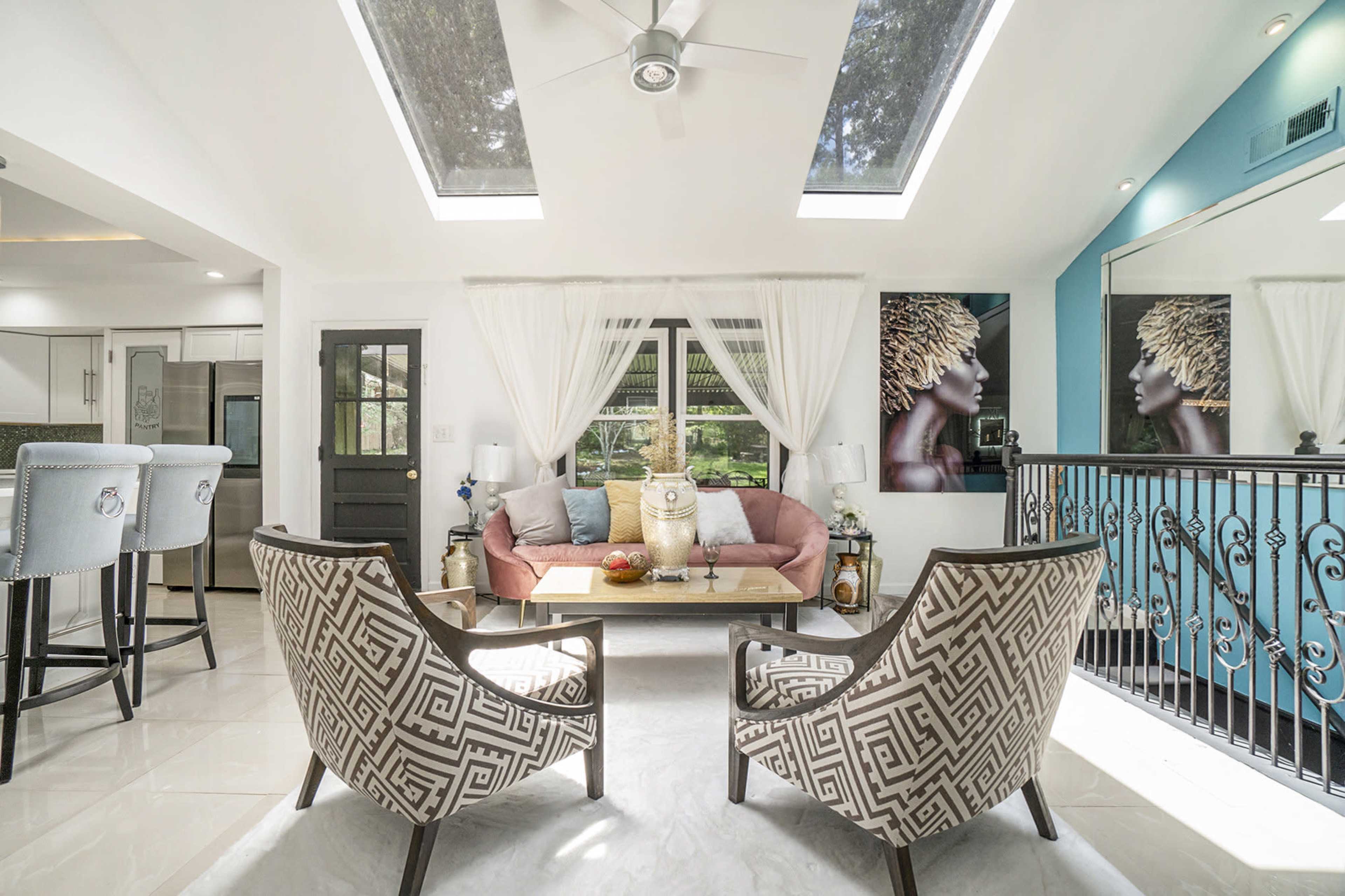 A modern living room with a pink couch, two patterned chairs, and large skylights letting in natural light.