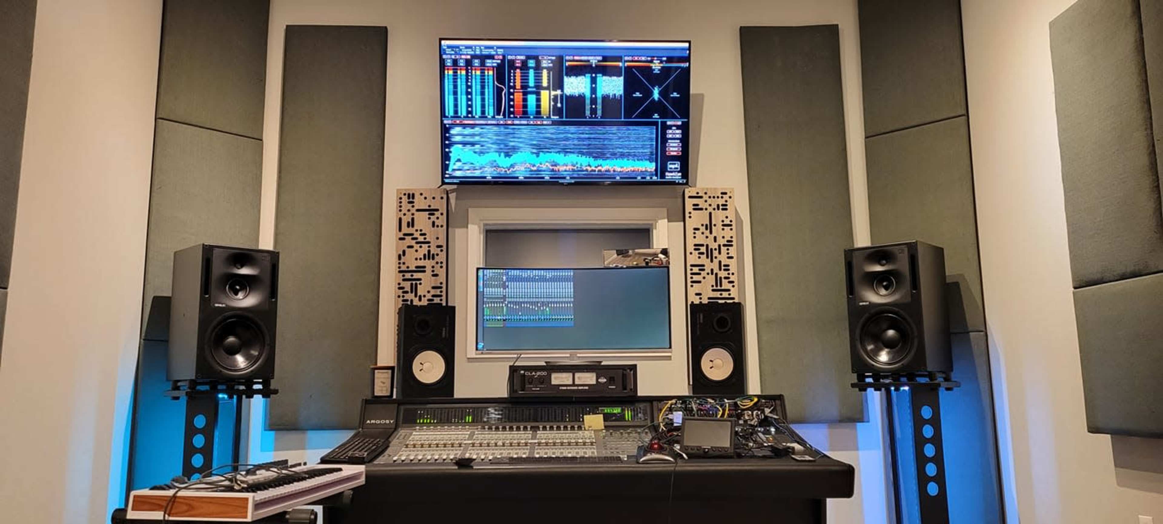 A music studio with a sound mixing console, computer monitors, and soundproofing panels on the walls.