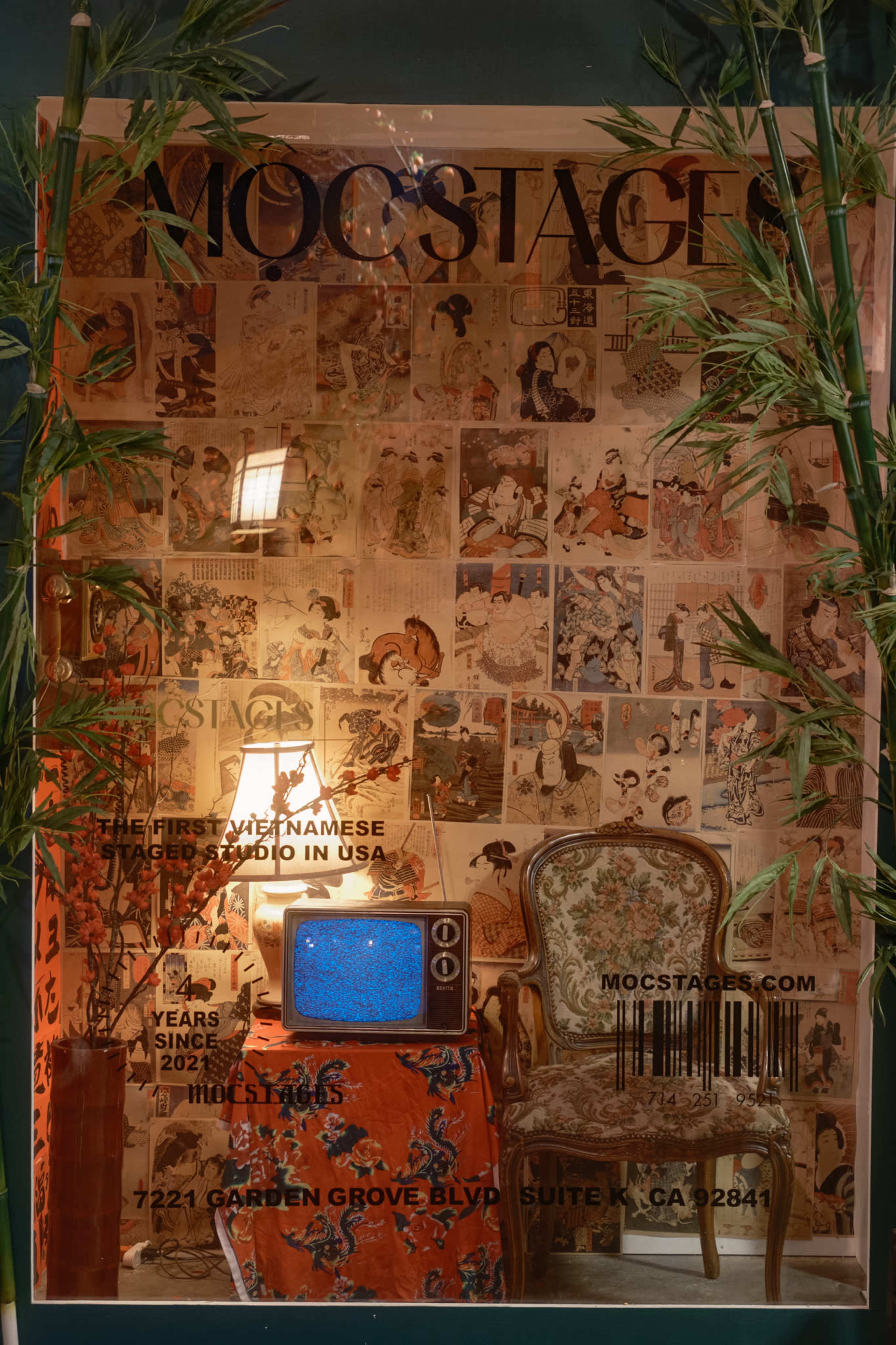 The image features a cozy corner with a vintage armchair beside a glowing lamp and an old television, set against a wall adorned with colorful posters and bamboo plants.