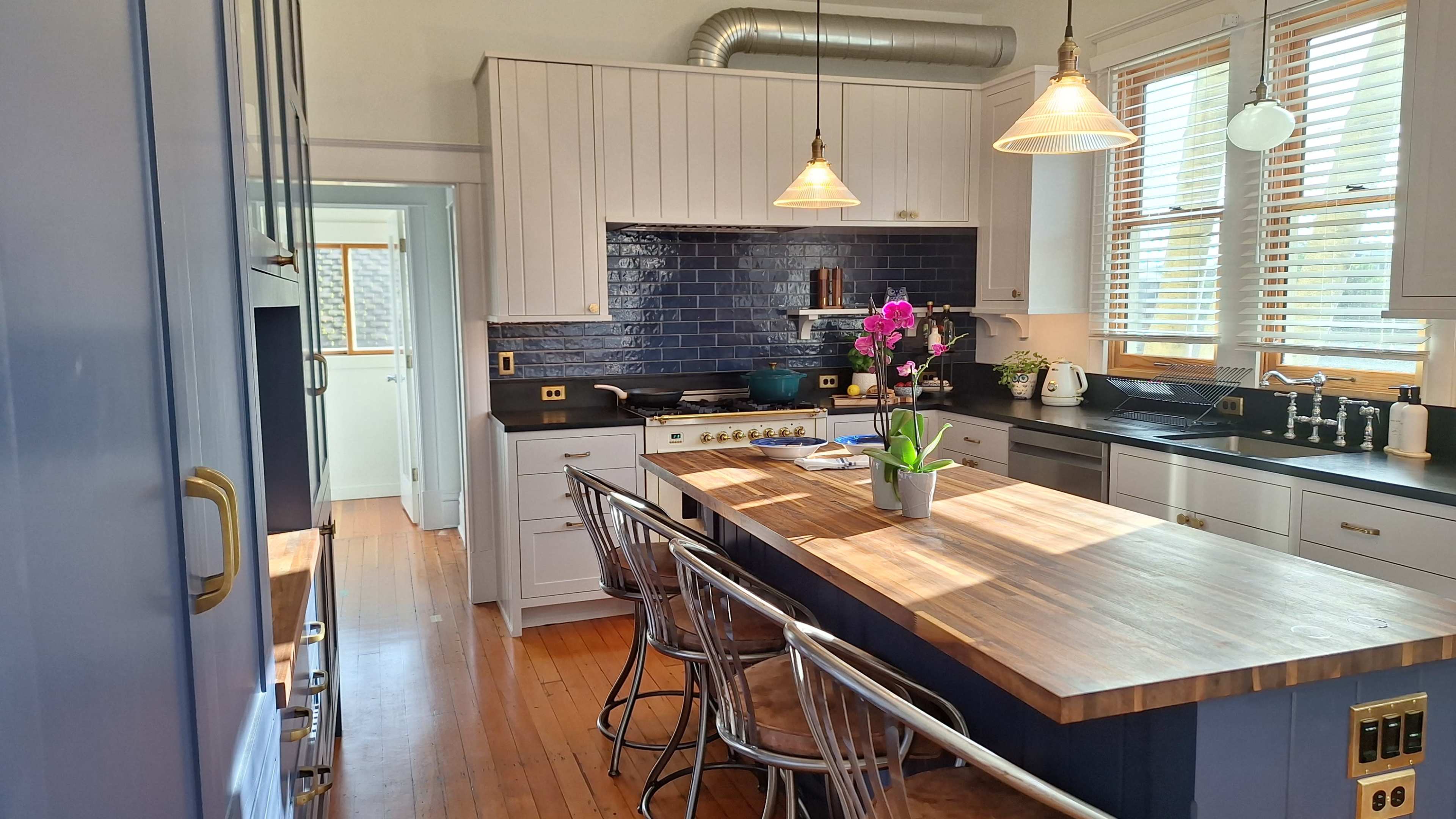 The image shows a modern kitchen featuring a central island with a wooden countertop, stainless steel appliances, and blue tile backsplash.