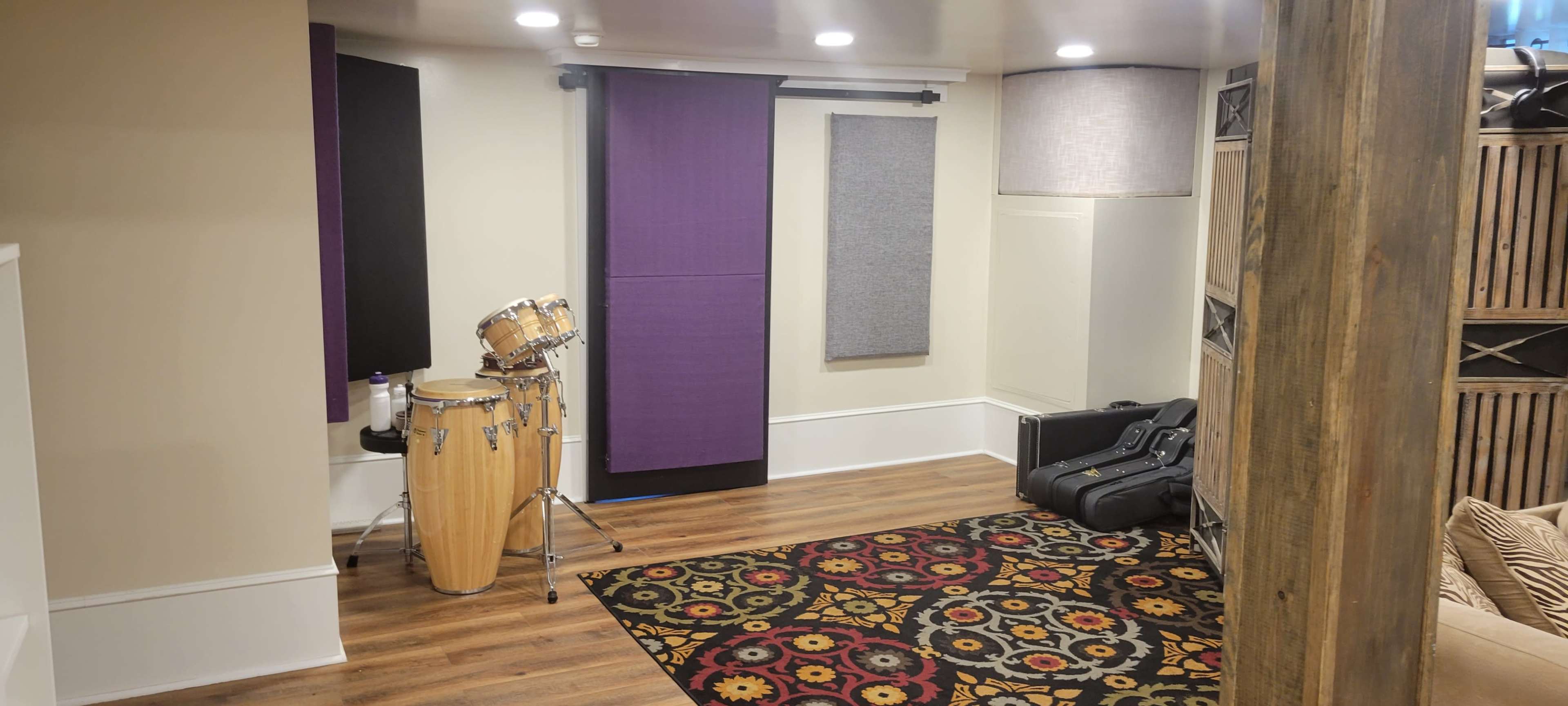 A music practice room featuring a conga drum set, acoustic panels on the walls, and a patterned rug on the floor.