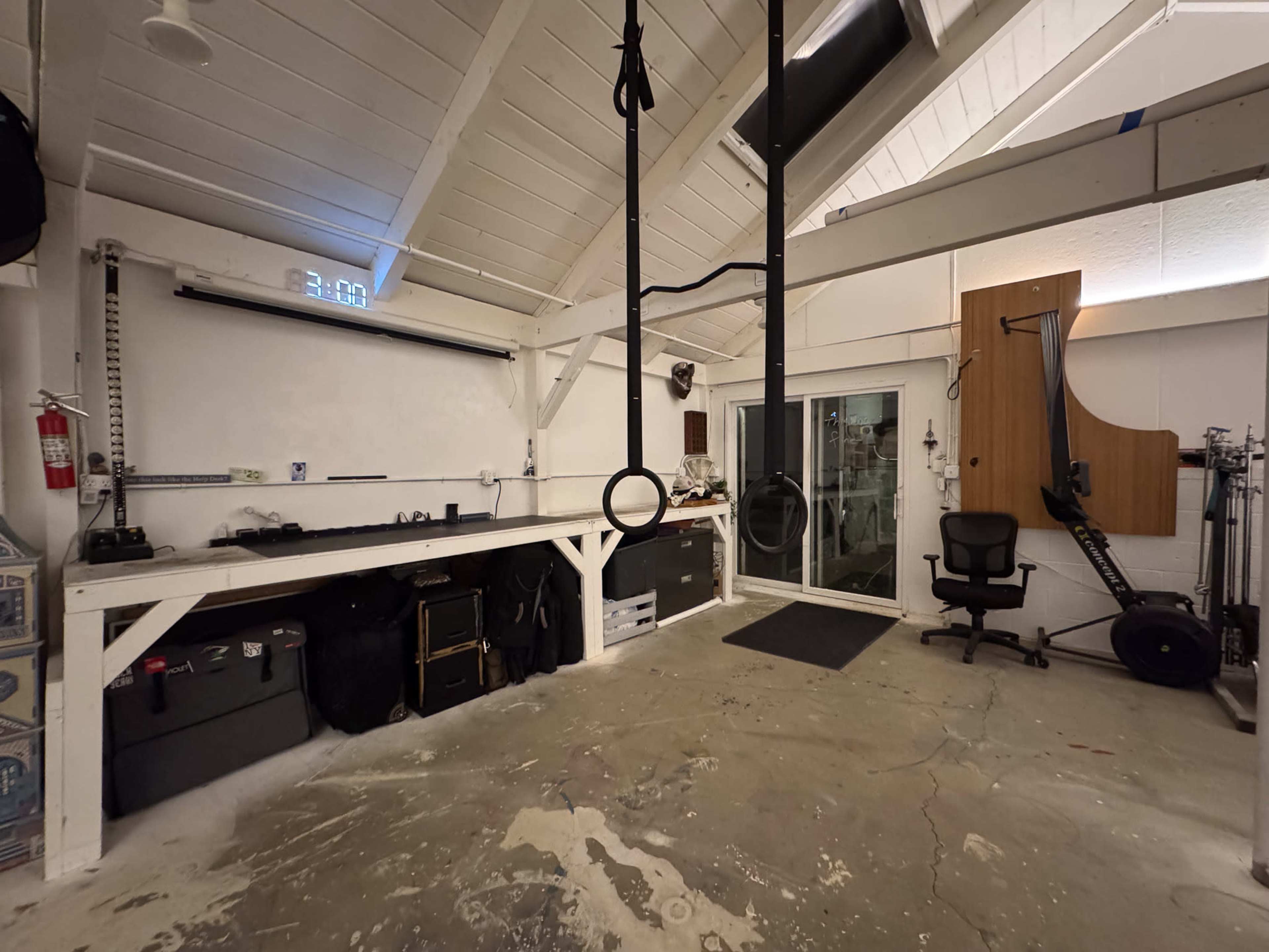 The image shows a spacious gym interior with workout rings hanging from the ceiling, a large whiteboard, and various fitness equipment arranged around the room.