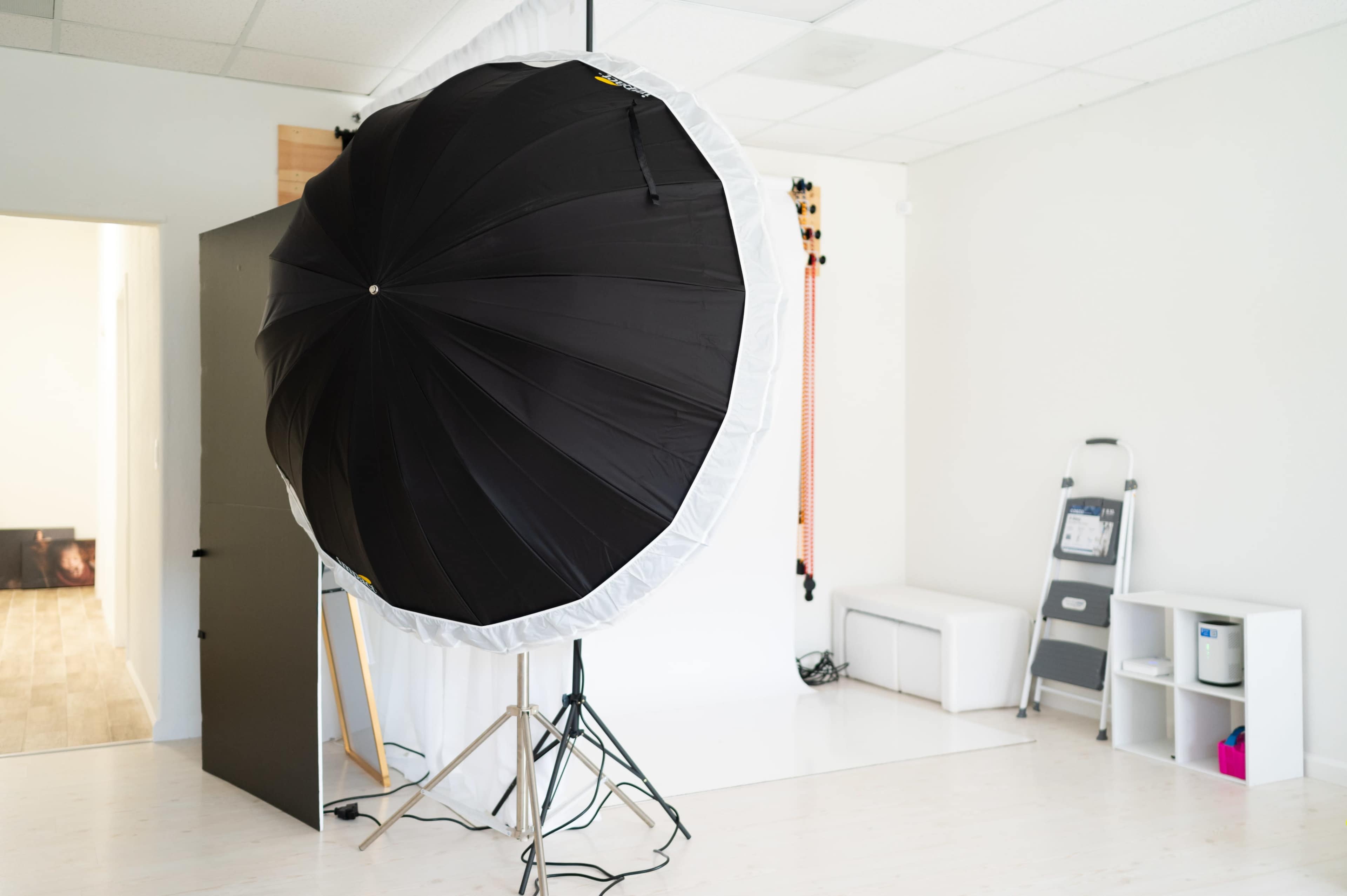 A large black and white umbrella light stands on a tripod in a bright, empty photography studio.