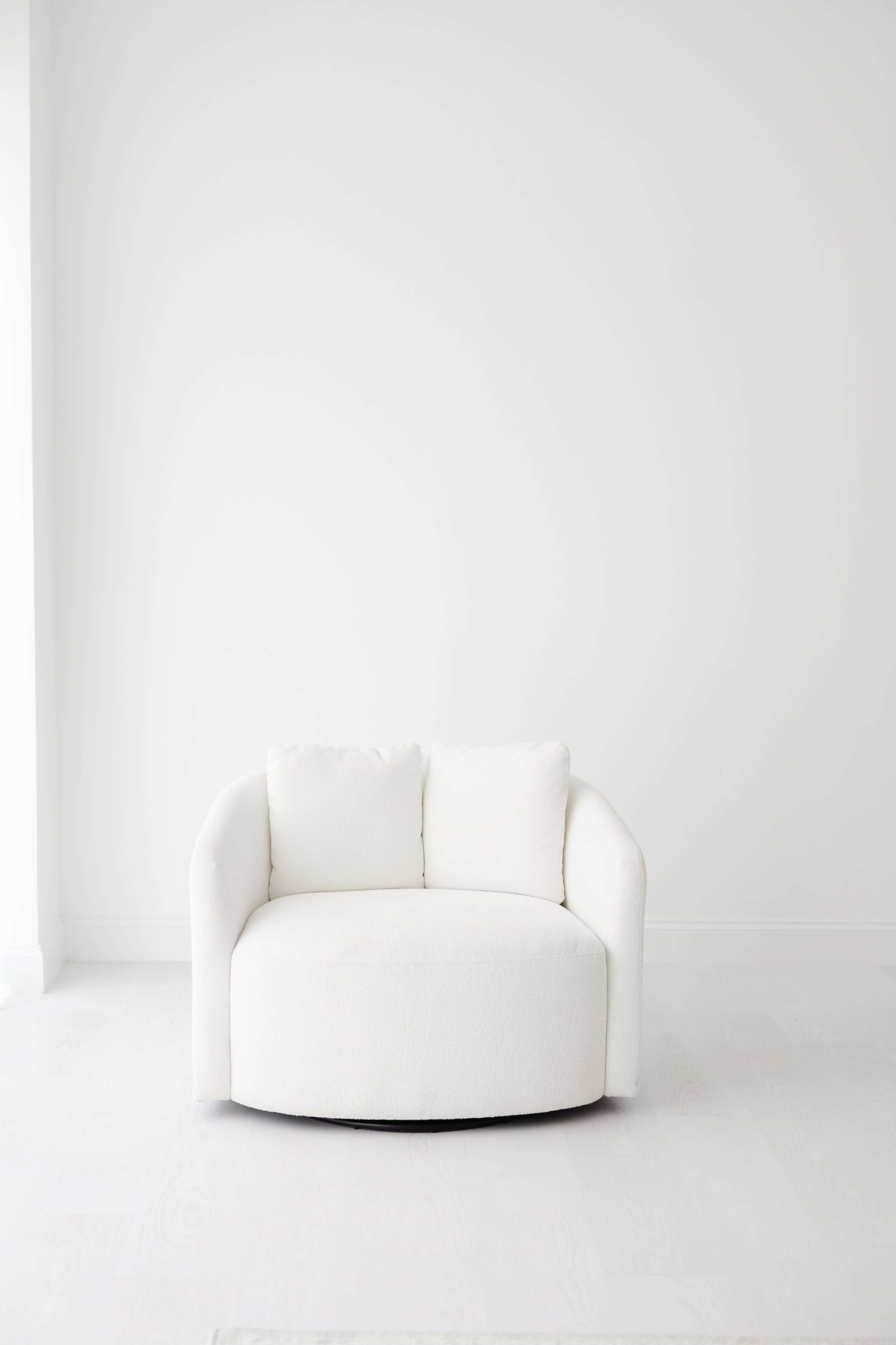A round, white upholstered chair with two armrests sits against a plain white wall.