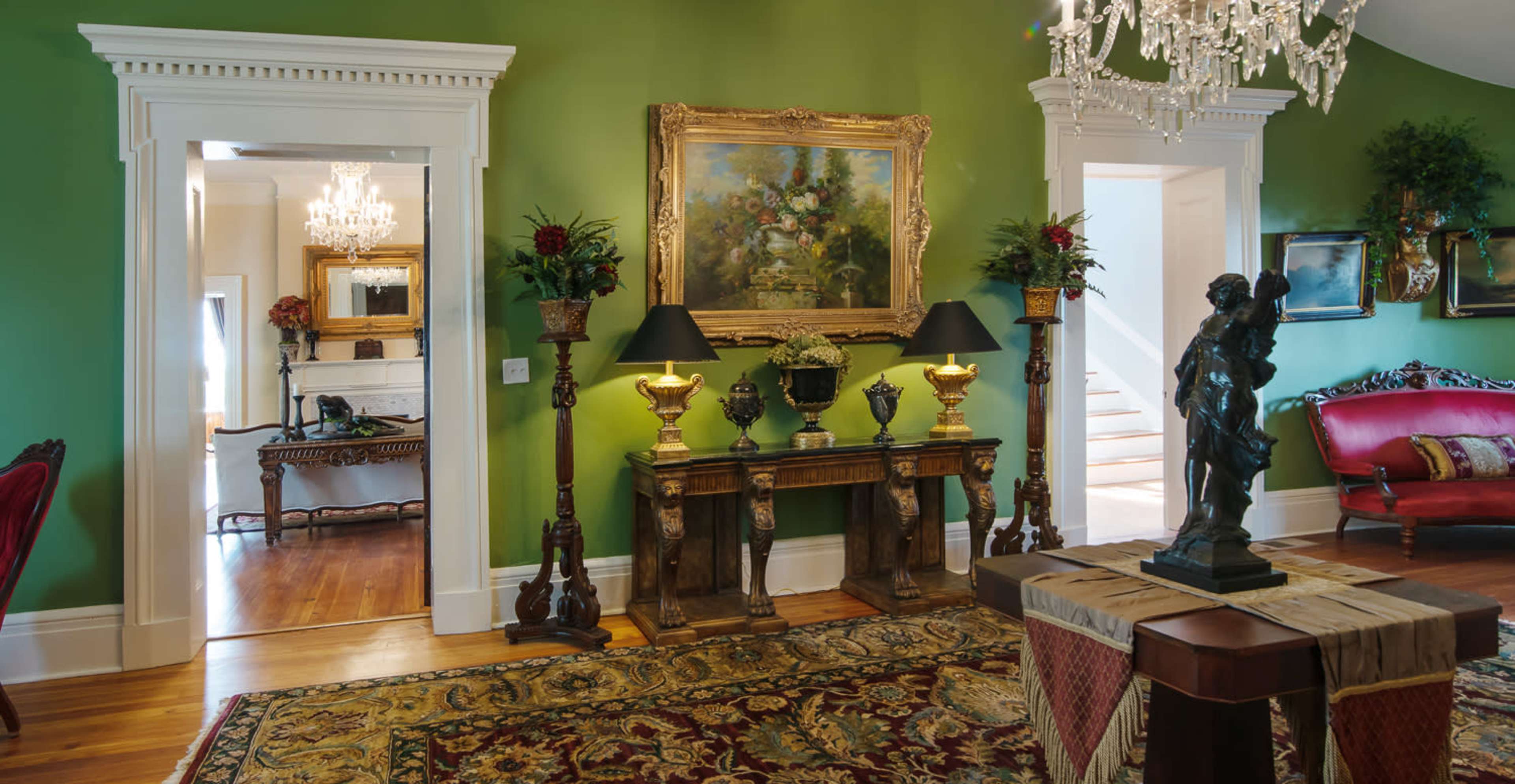 A lavishly decorated interior with green walls, ornate furniture, and a staircase in the background.